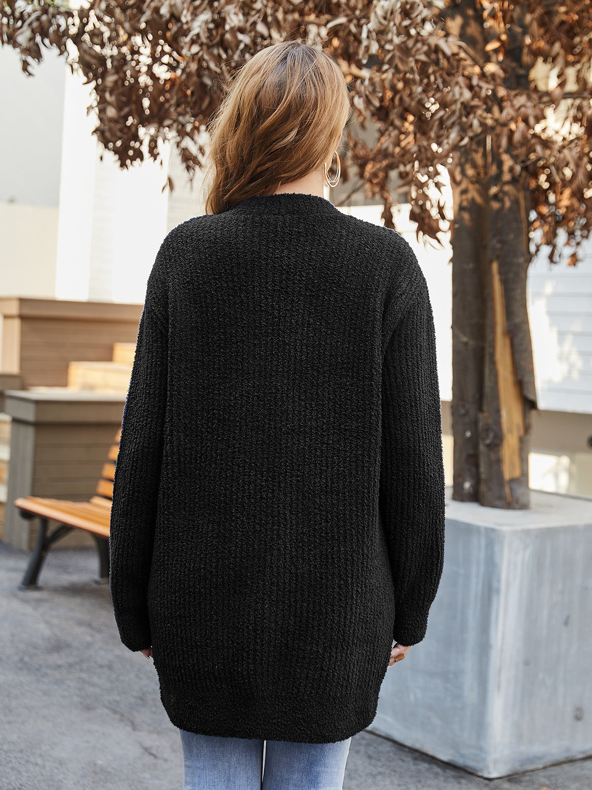 Person wearing a black sweater standing outdoors with trees and a bench in the background #color_Black