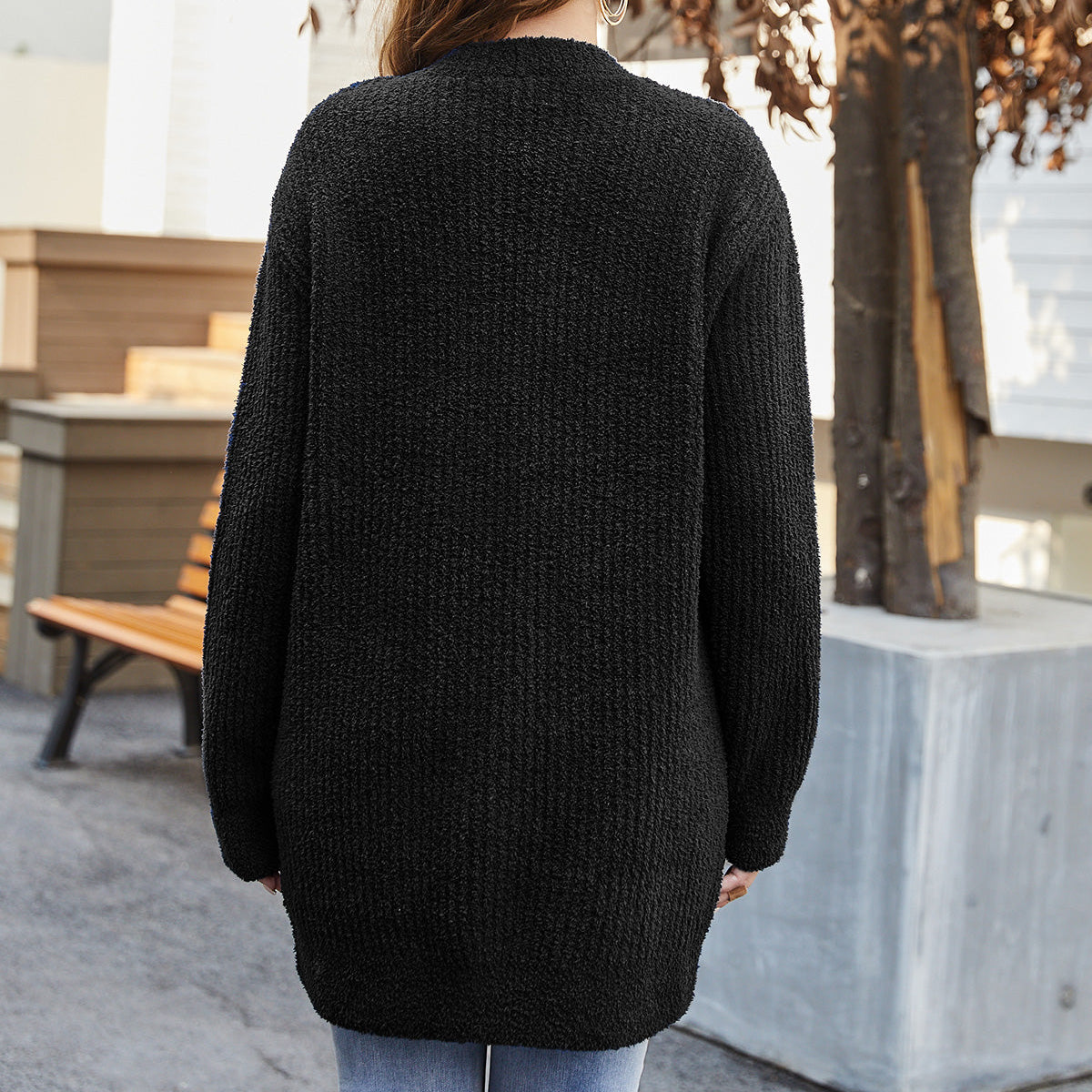 Person wearing a black sweater standing outdoors with trees and a bench in the background #color_Black