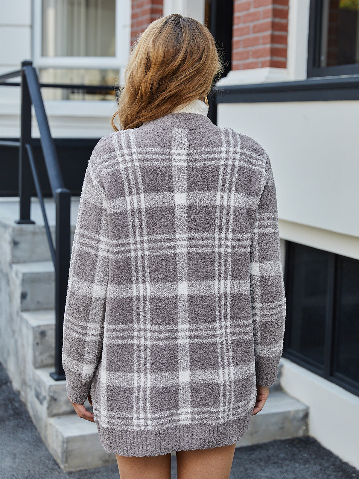 Person wearing a gray and white plaid cardigan standing on a porch. #color_Taupe Check