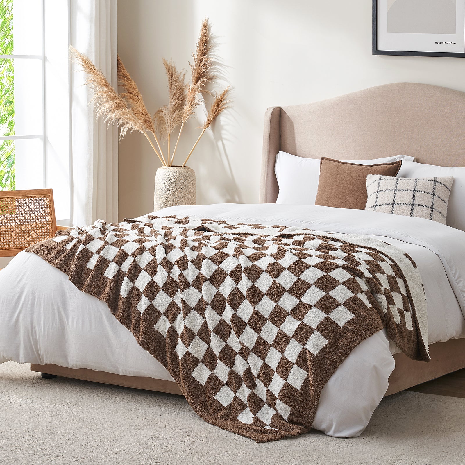 Bedroom with a bed featuring a brown and white checkered blanket, pillows, and a vase with pampas grass. #color_Checkered Brown