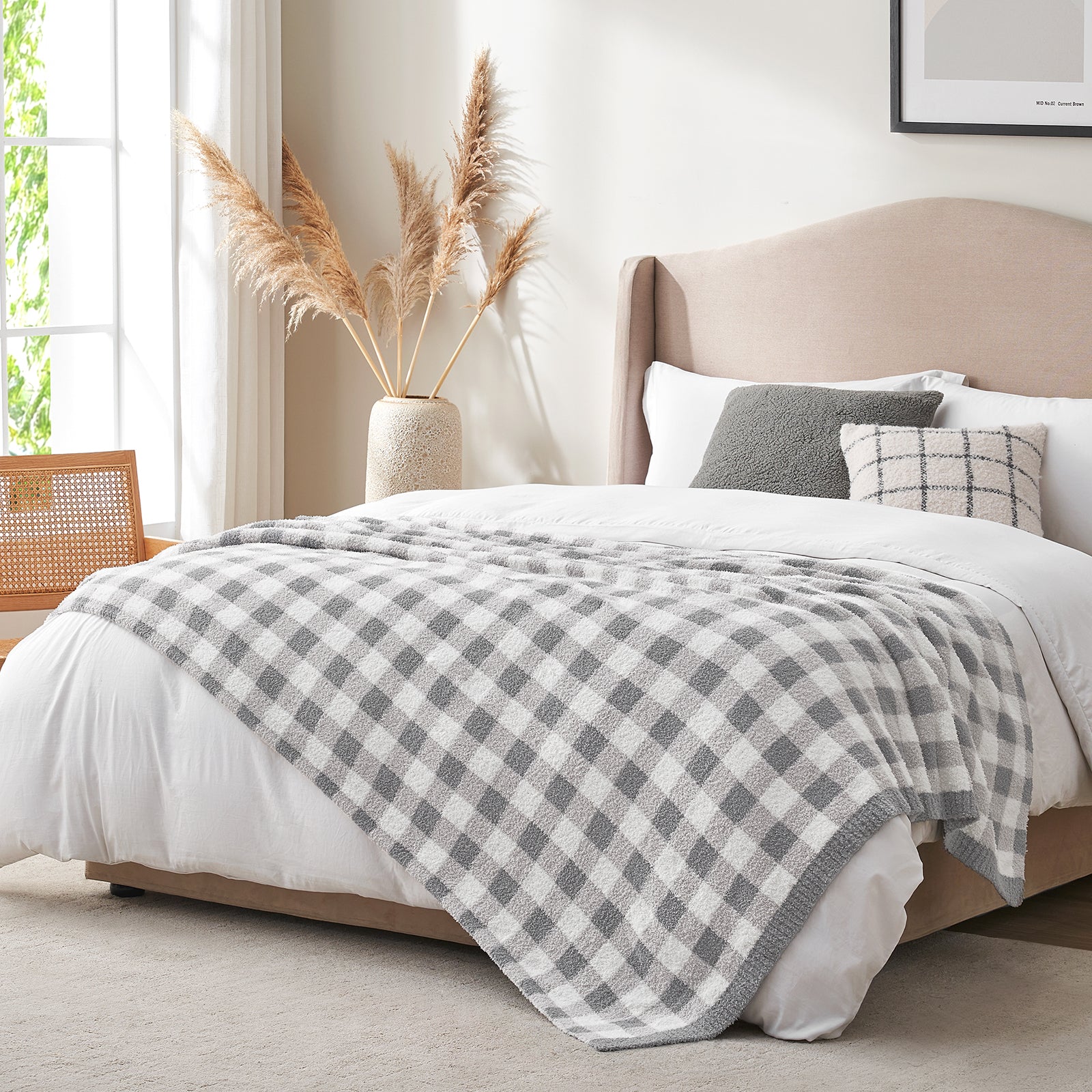 Bedroom with a bed covered in a gray and white checkered blanket, pillows, and a vase with pampas grass. #color_Plaid Grey