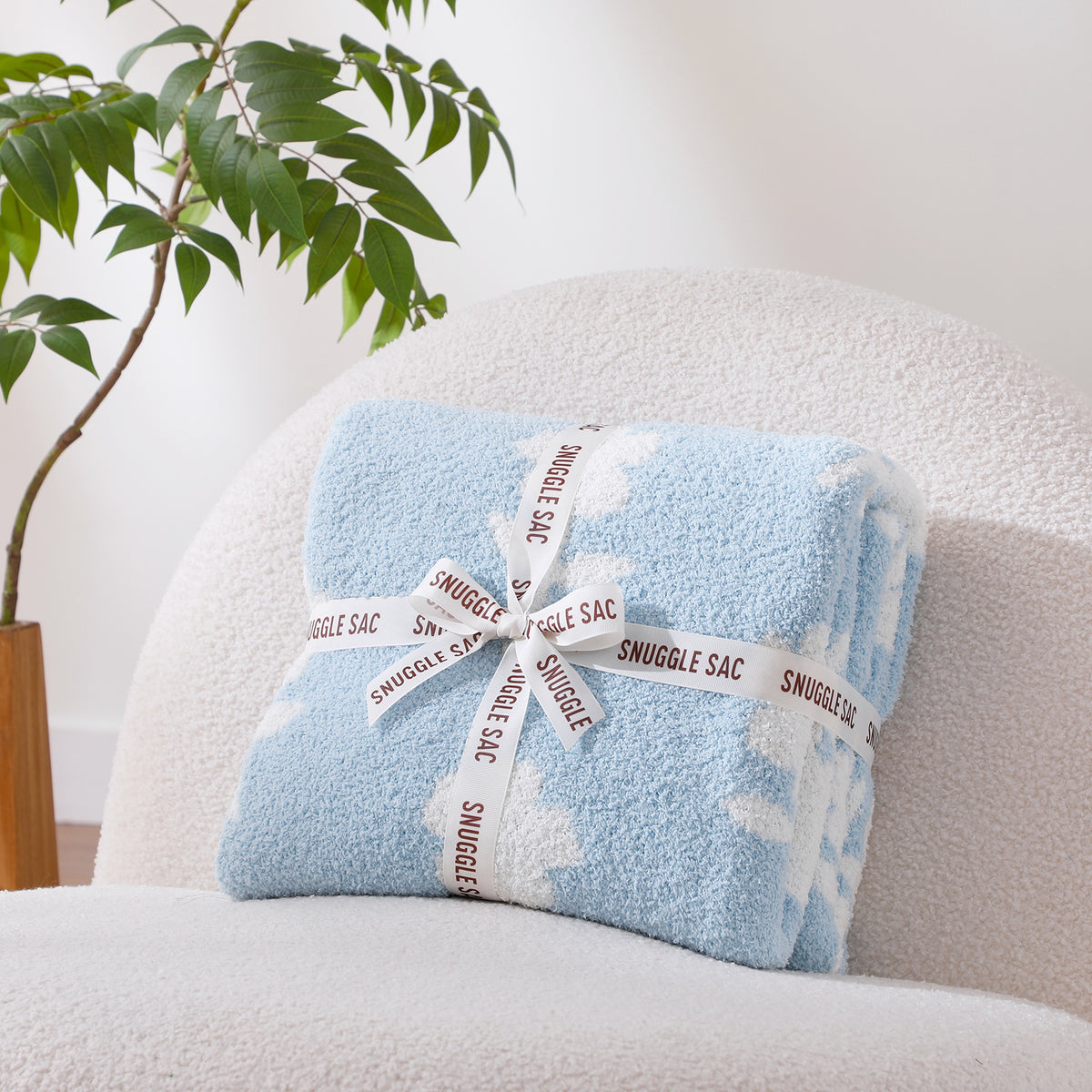 Folded flower blanket with 'Snuggle Sac' branding on a blue surface, accompanied by decorative flower print. #color_Sky Blue