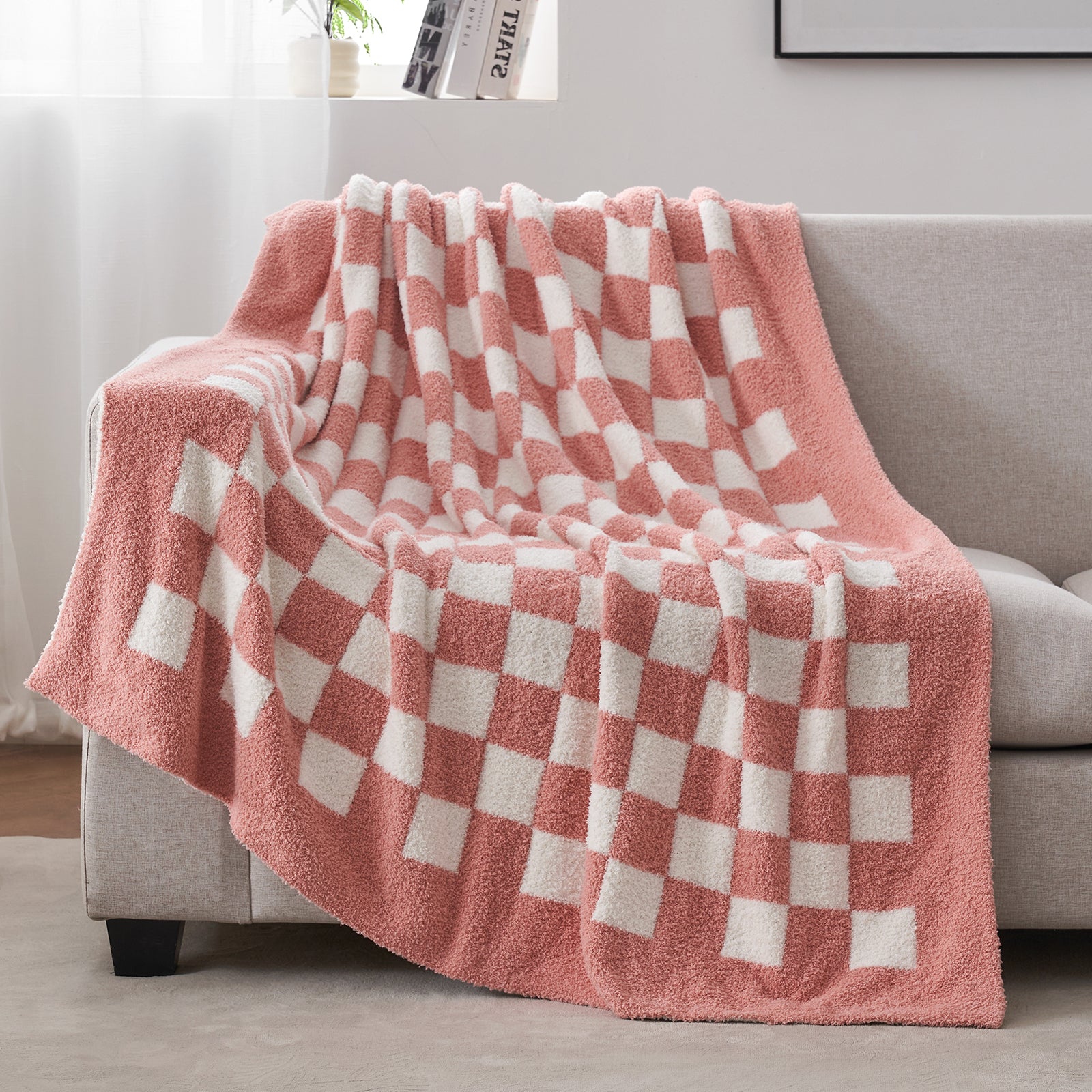 Pink and white checkered blanket draped over a gray sofa in a living room setting. #color_Checkered Pink