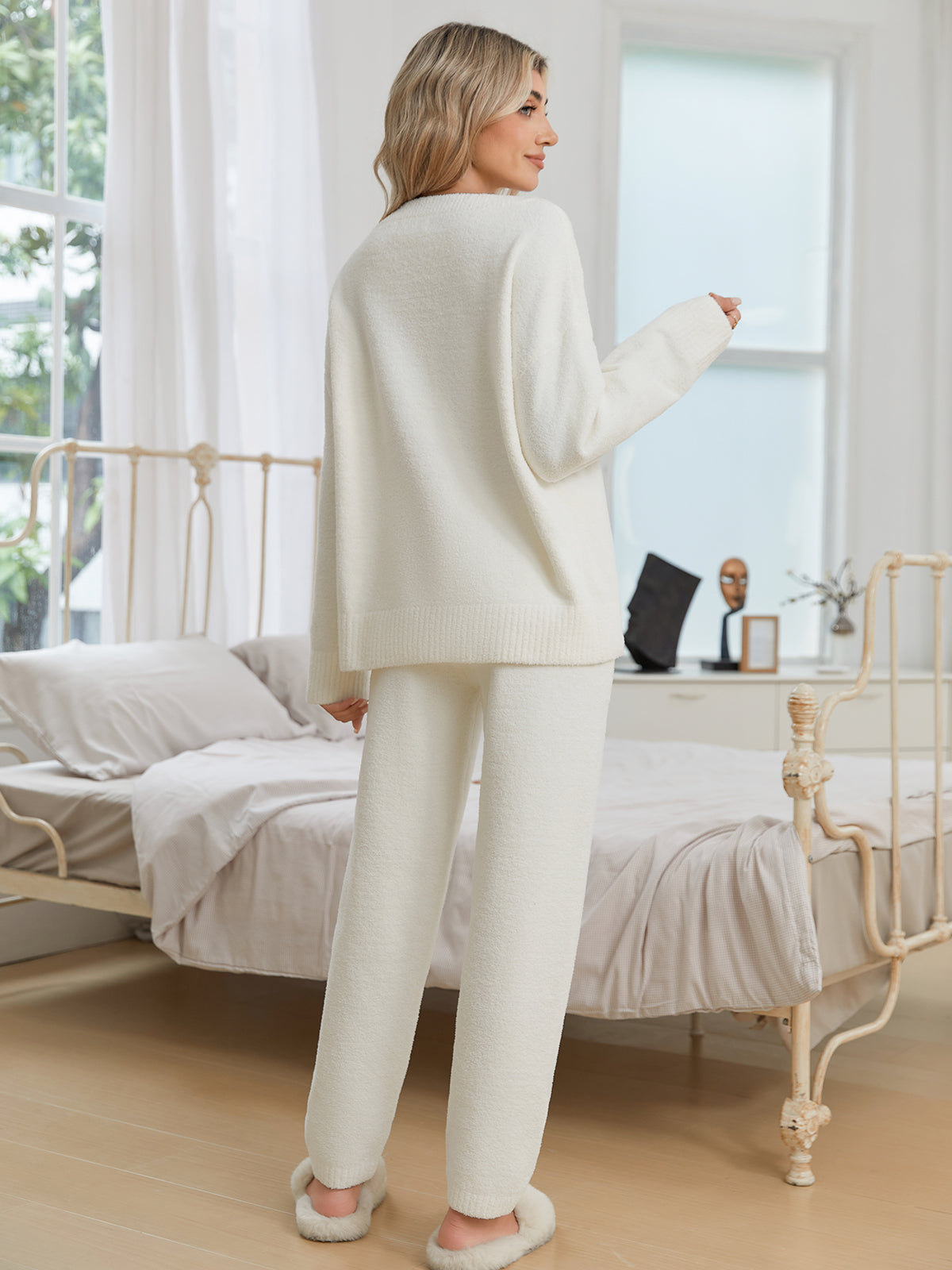 Woman in a white outfit standing in a bedroom with a desk and window in the background. #color_Ivory