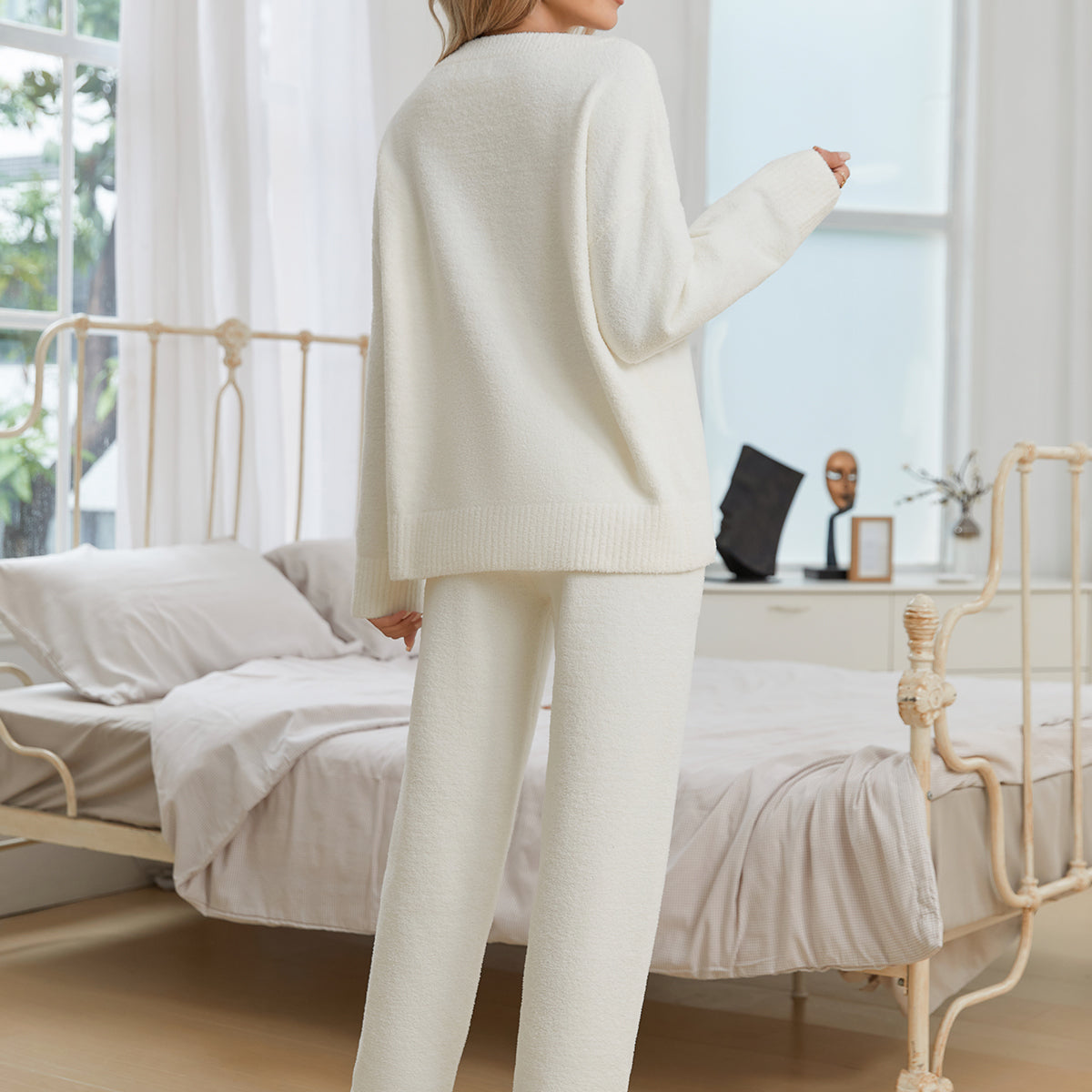 Woman in a white outfit standing in a bedroom with a desk and window in the background. #color_Ivory