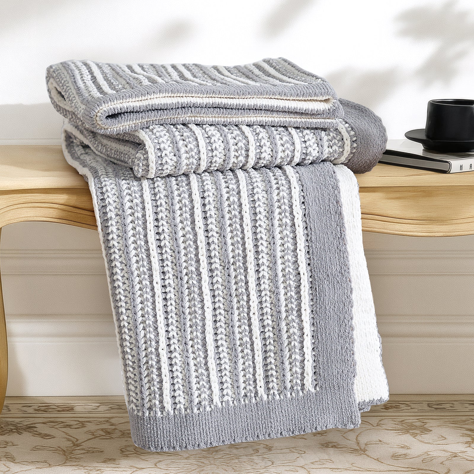 Snuggle Sac gray and white striped blanket on a wooden bench with a cup and book in the background. #color_Gray&White