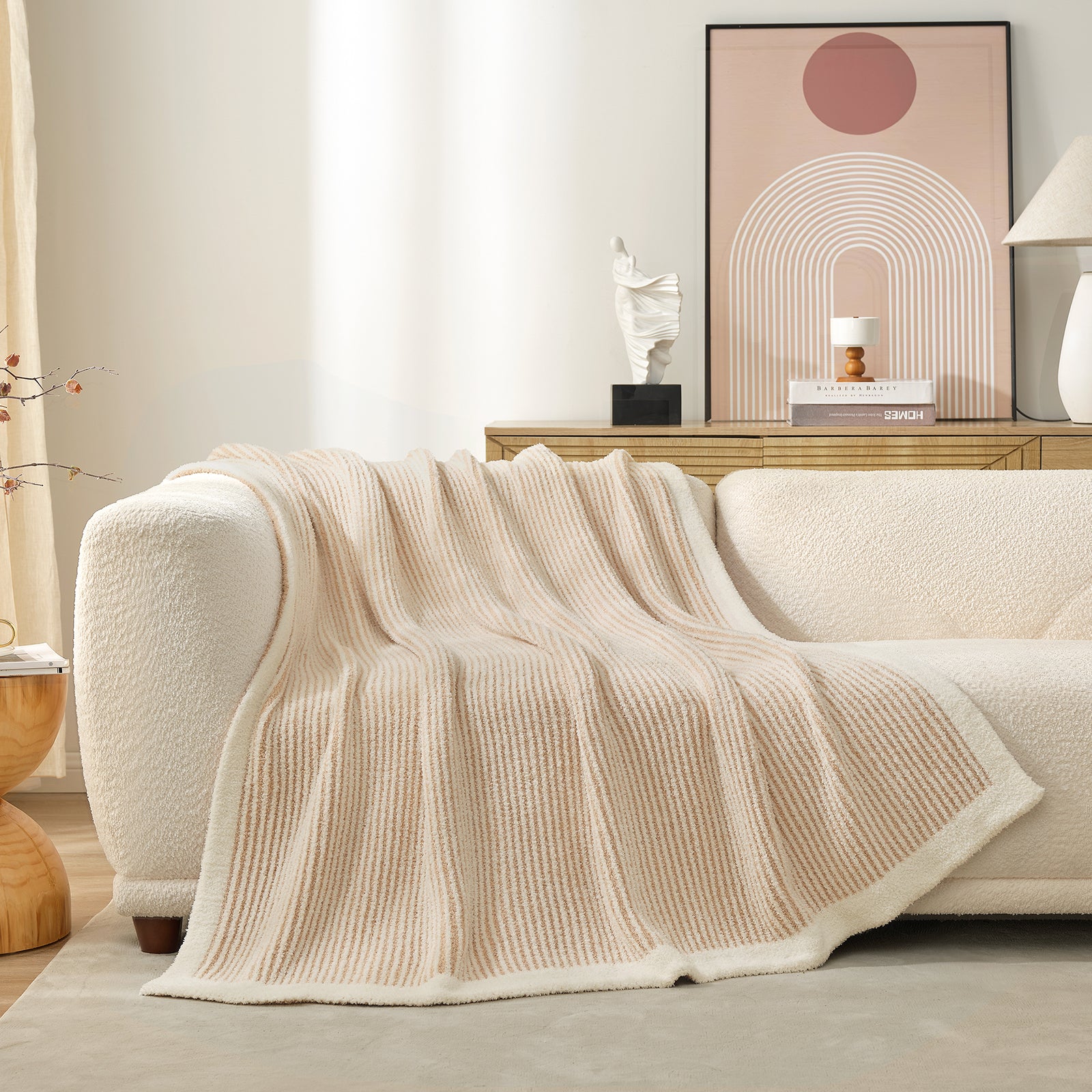 Beige knitted blanket draped over a white sofa in a living room setting.#color_Cream/Beige