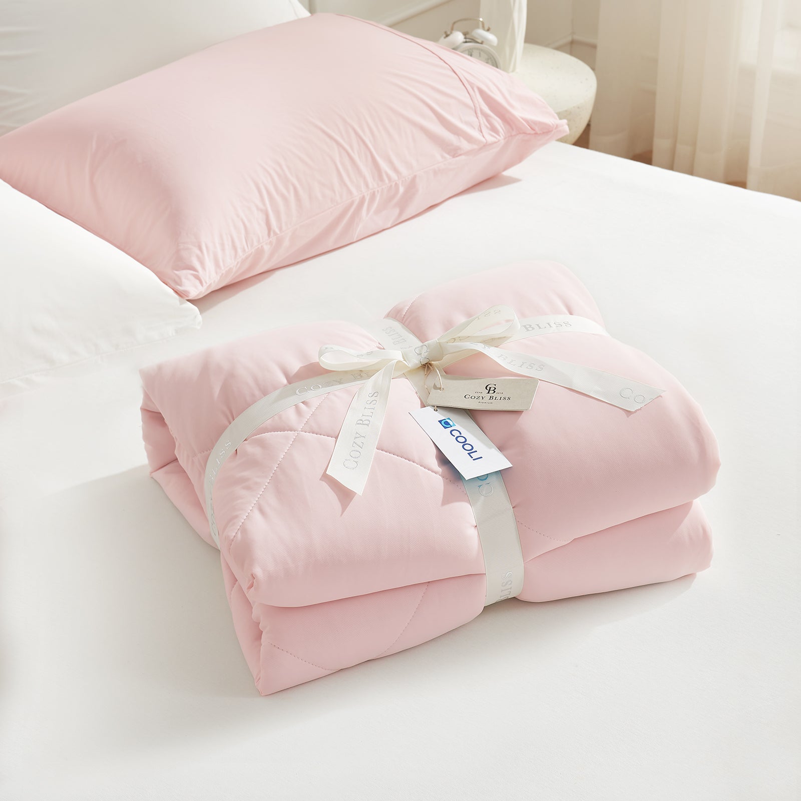 Cooling comforter with a white ribbon on bed, perfect as gift.#color_Pink/Grey