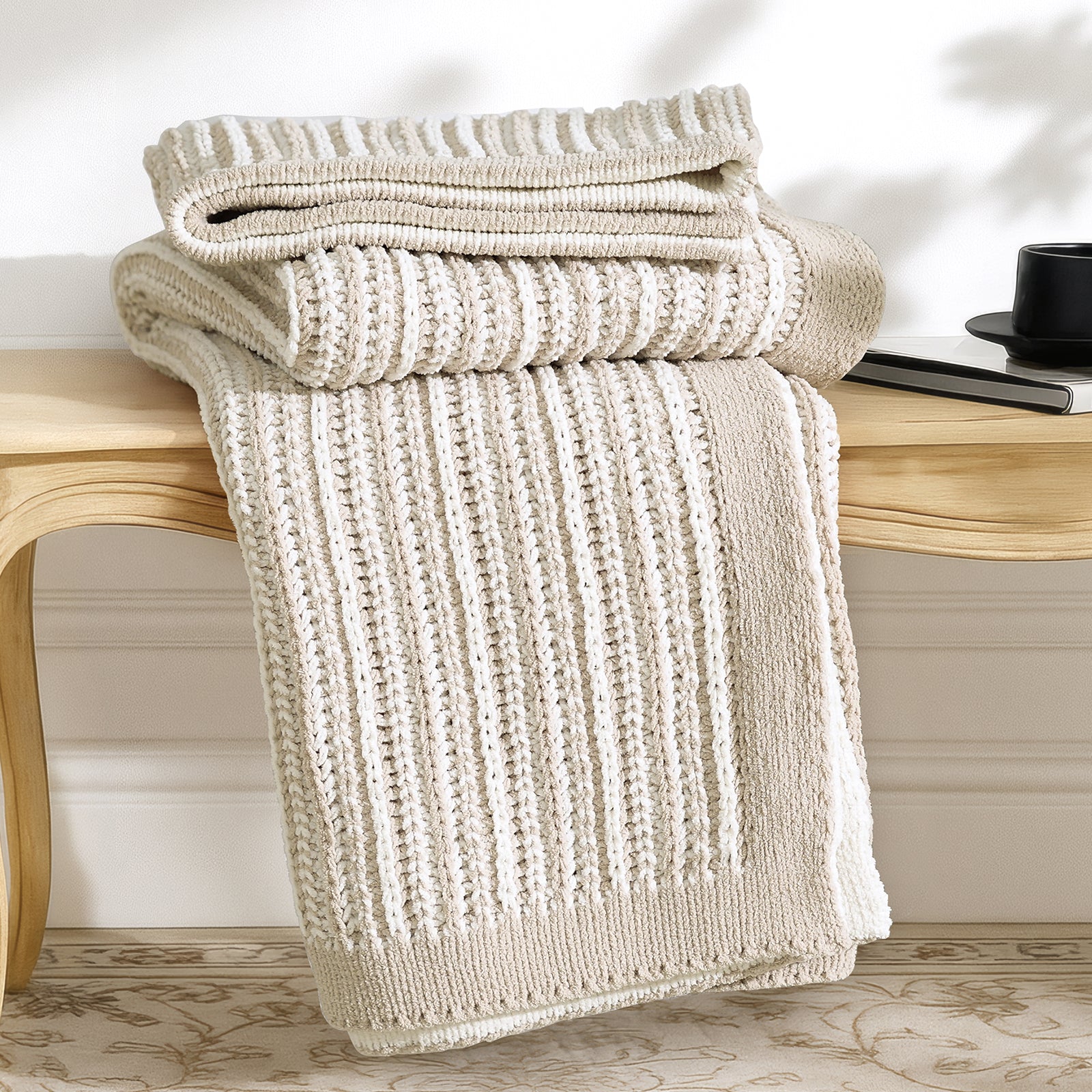 Snuggle Sac beige knitted blanket draped over a wooden bench with a blurred background #color_Khaki&White