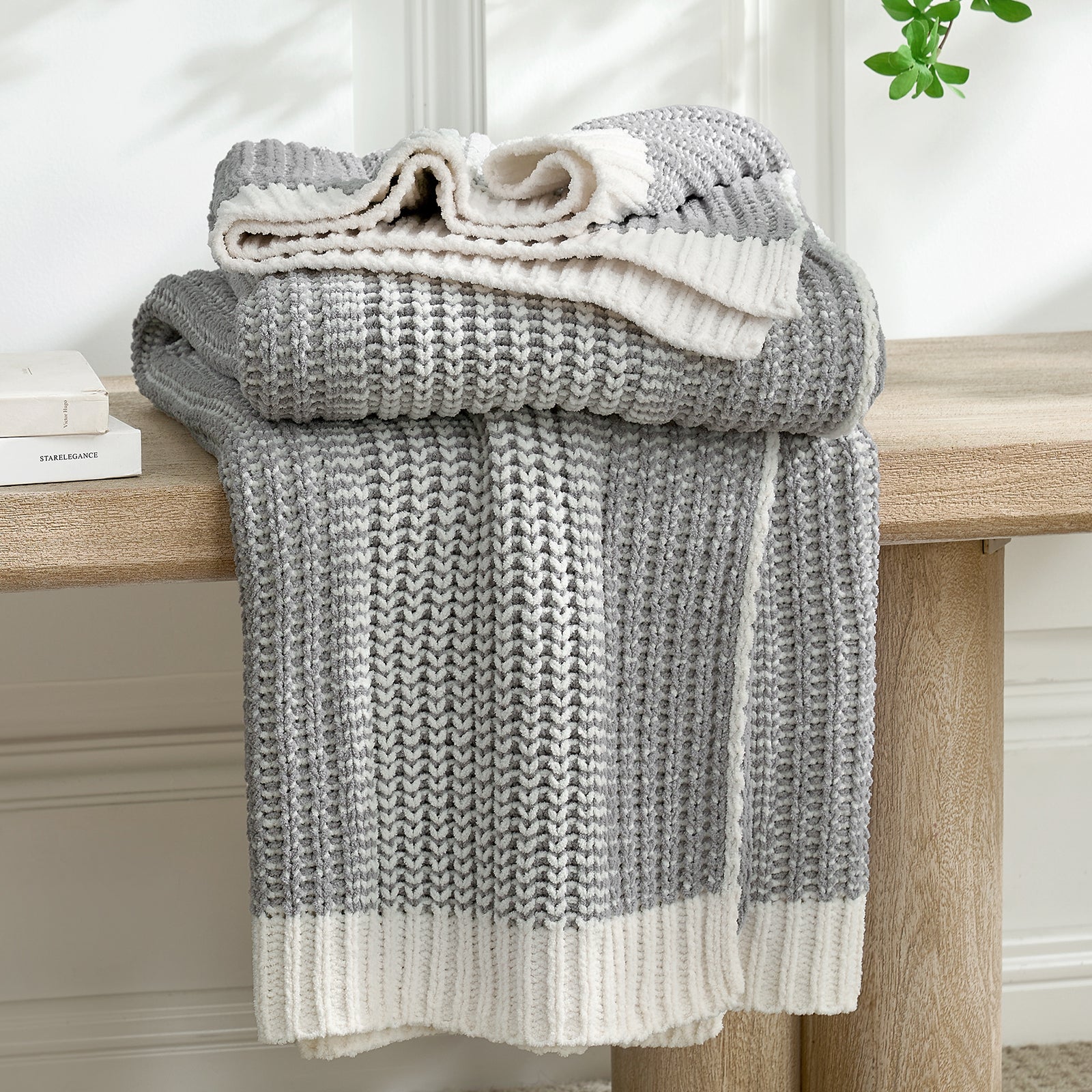 Snuggle Sac grey and white knitted blanket draped over a wooden bench with a neutral background #color_Two-tone Grey