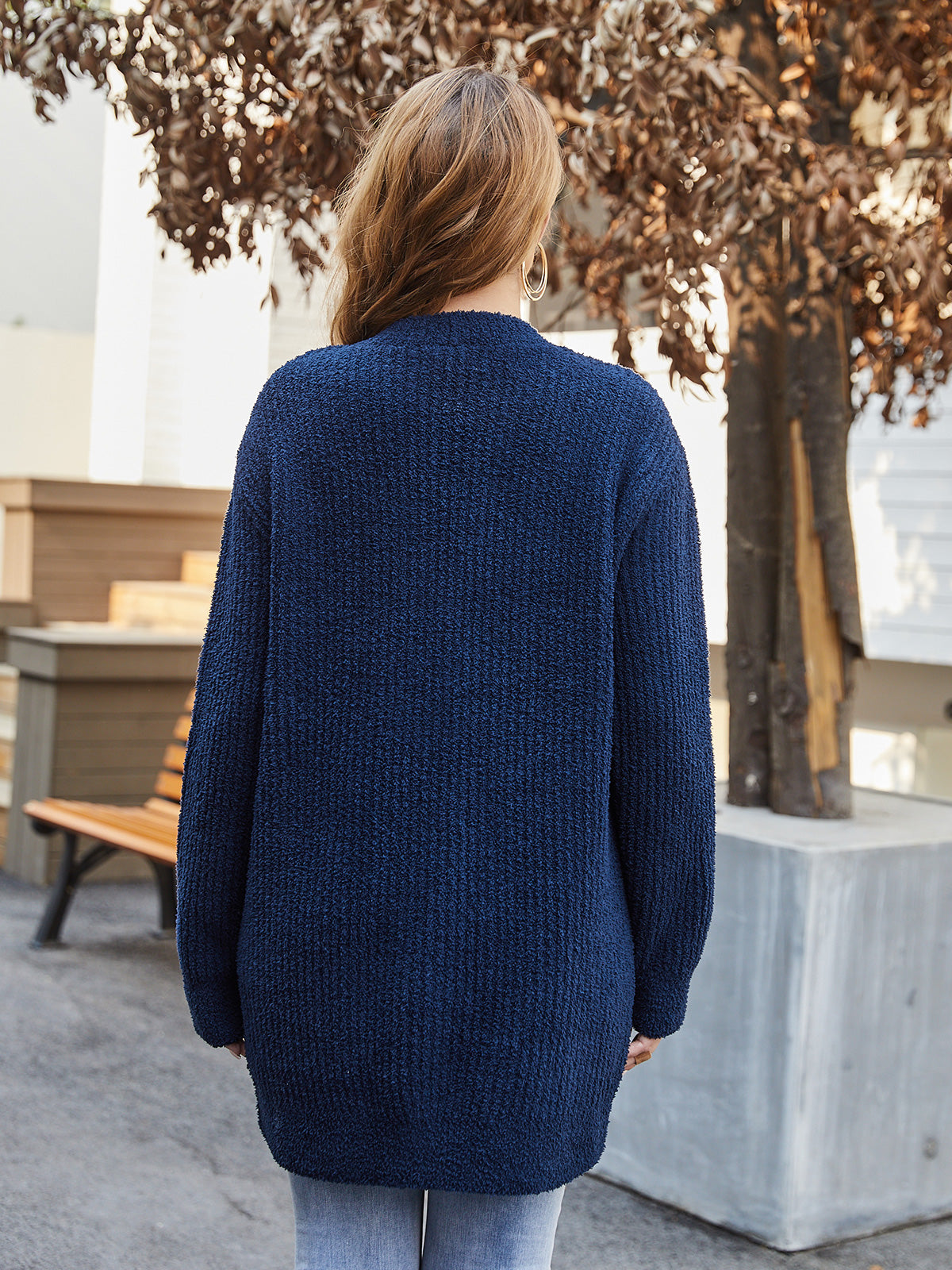 Person wearing a blue cardigan standing outdoors with trees and a bench in the background #color_Navy Blue