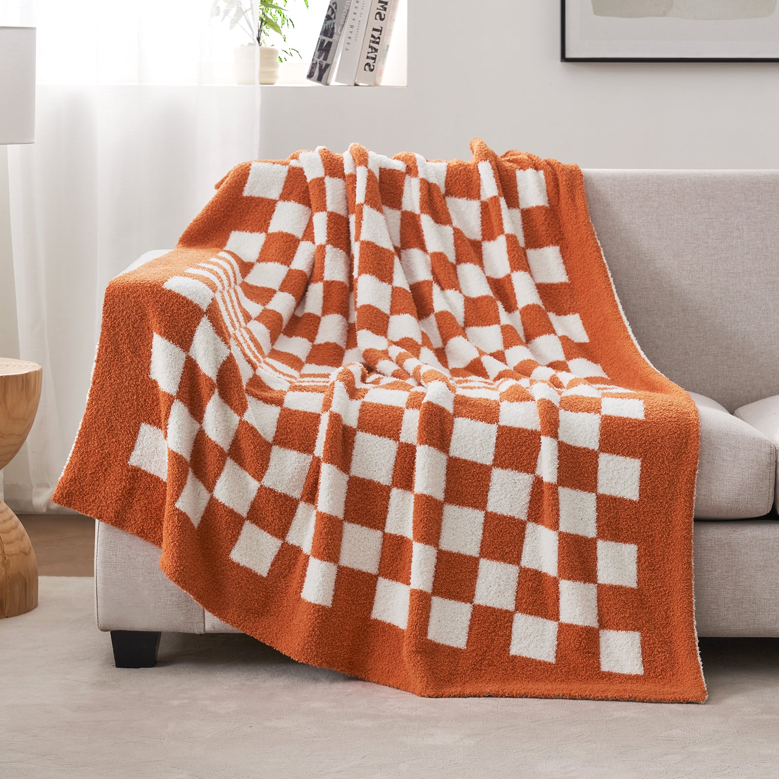 Orange and white checkered blanket draped over a sofa in a living room setting. #color_Checkered Burnt Orange