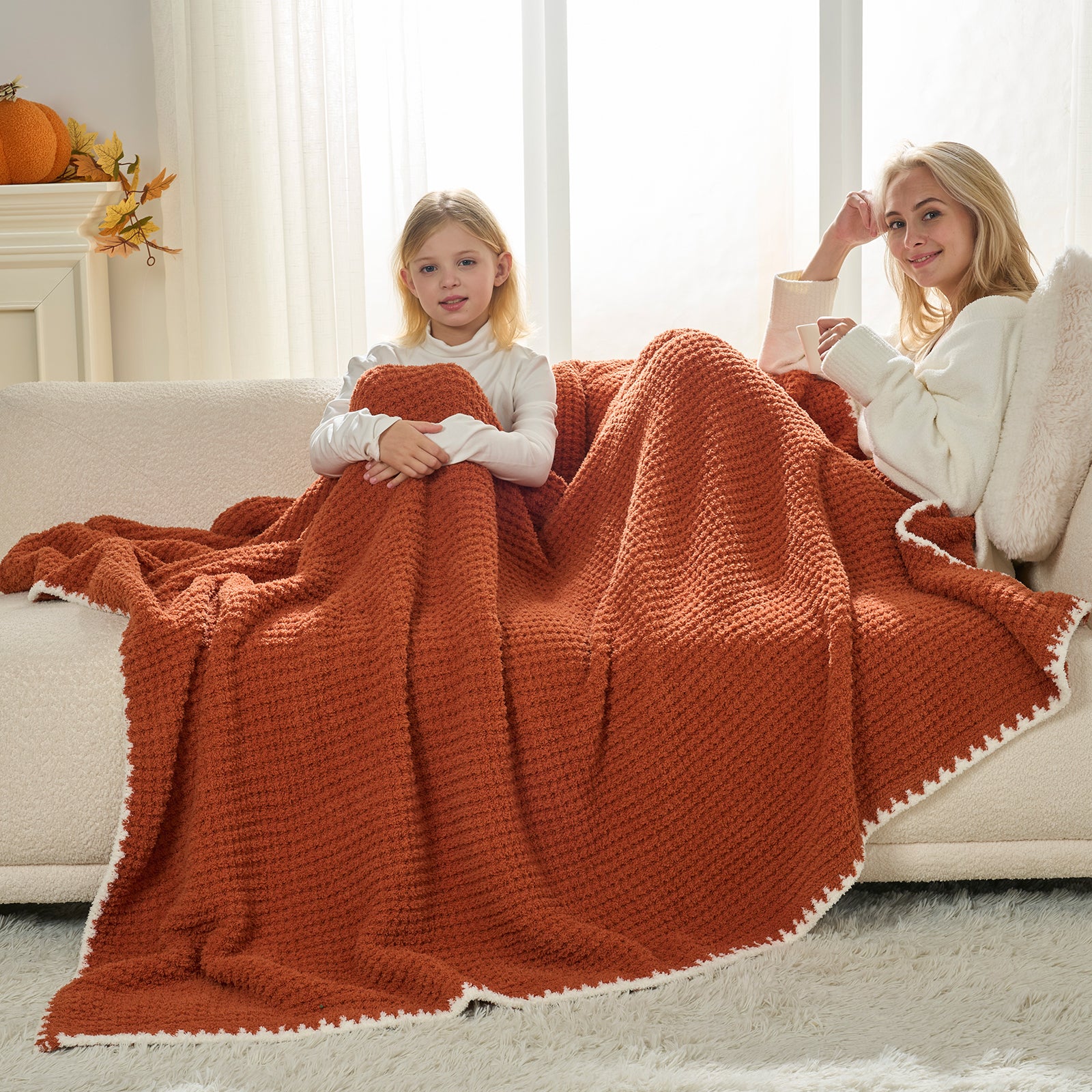 Two people sitting on a couch under a large orange blanket in a cozy living room.#color_Orange