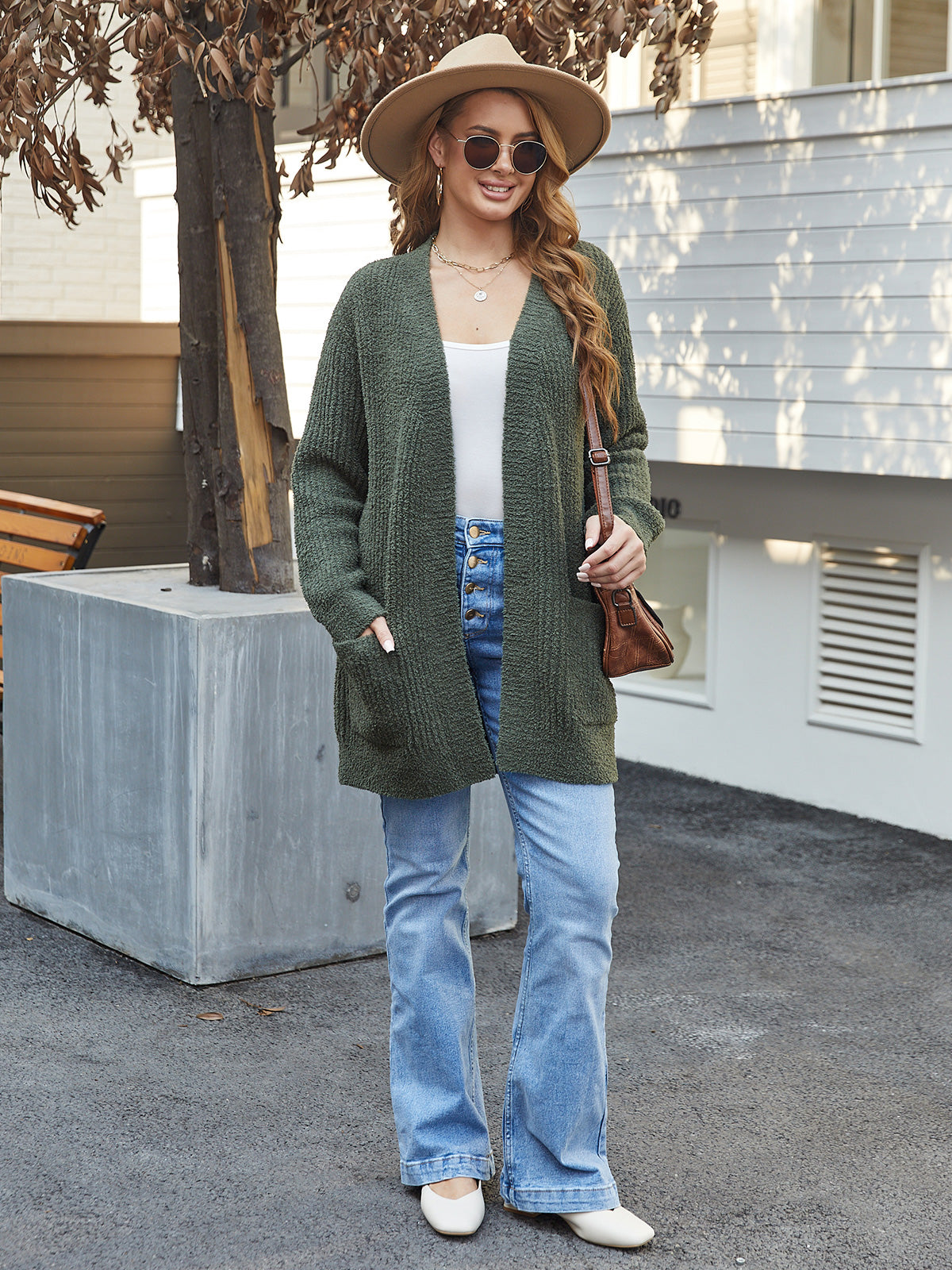 Woman wearing a green cardigan, white top, blue jeans, and a hat outdoors.#color_Army Green
