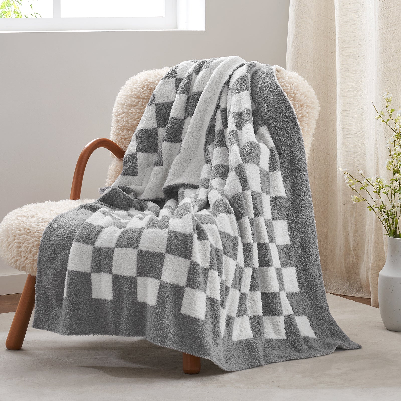 Gray and white checkered blanket draped over a chair in a room with a window and plant. #color_Checkered Grey