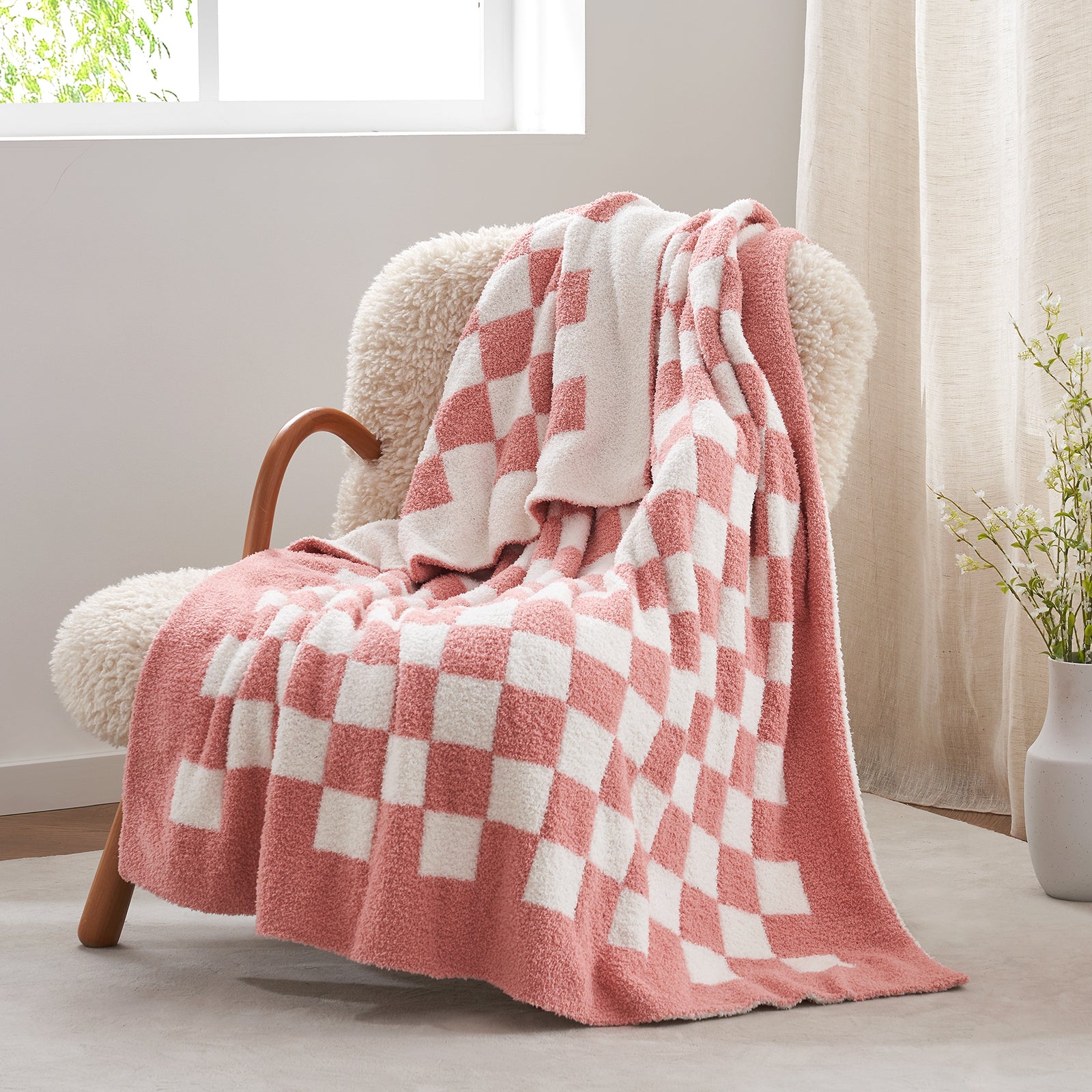 Pink and white checkered blanket draped over a chair in a bright room with a vase of flowers. #color_Checkered Pink