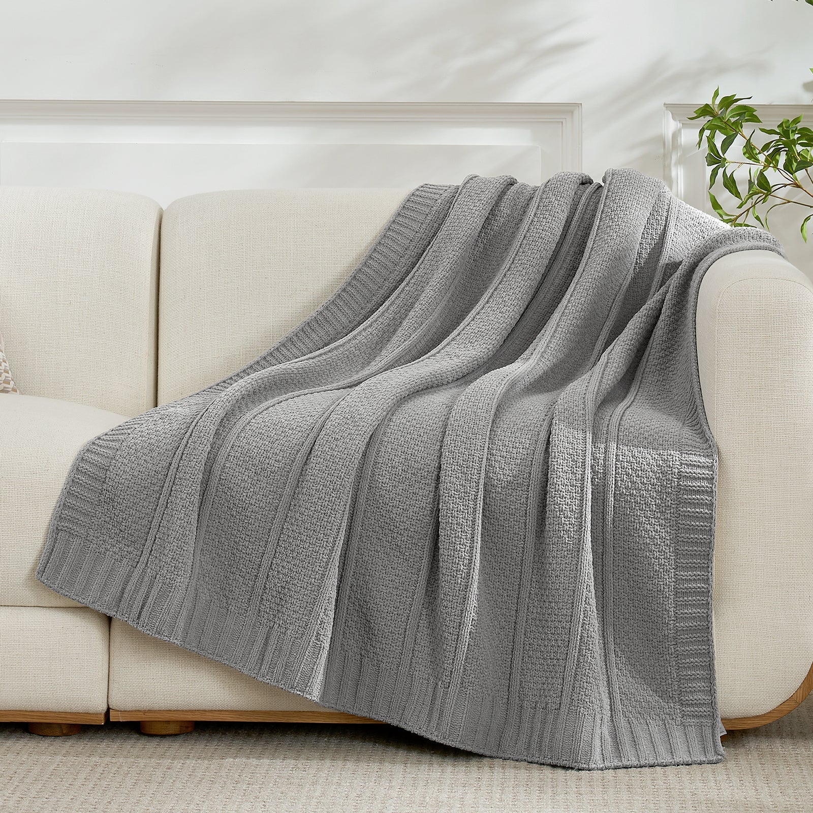 Gray textured blanket draped over a beige sofa in a living room setting. #color_Gray