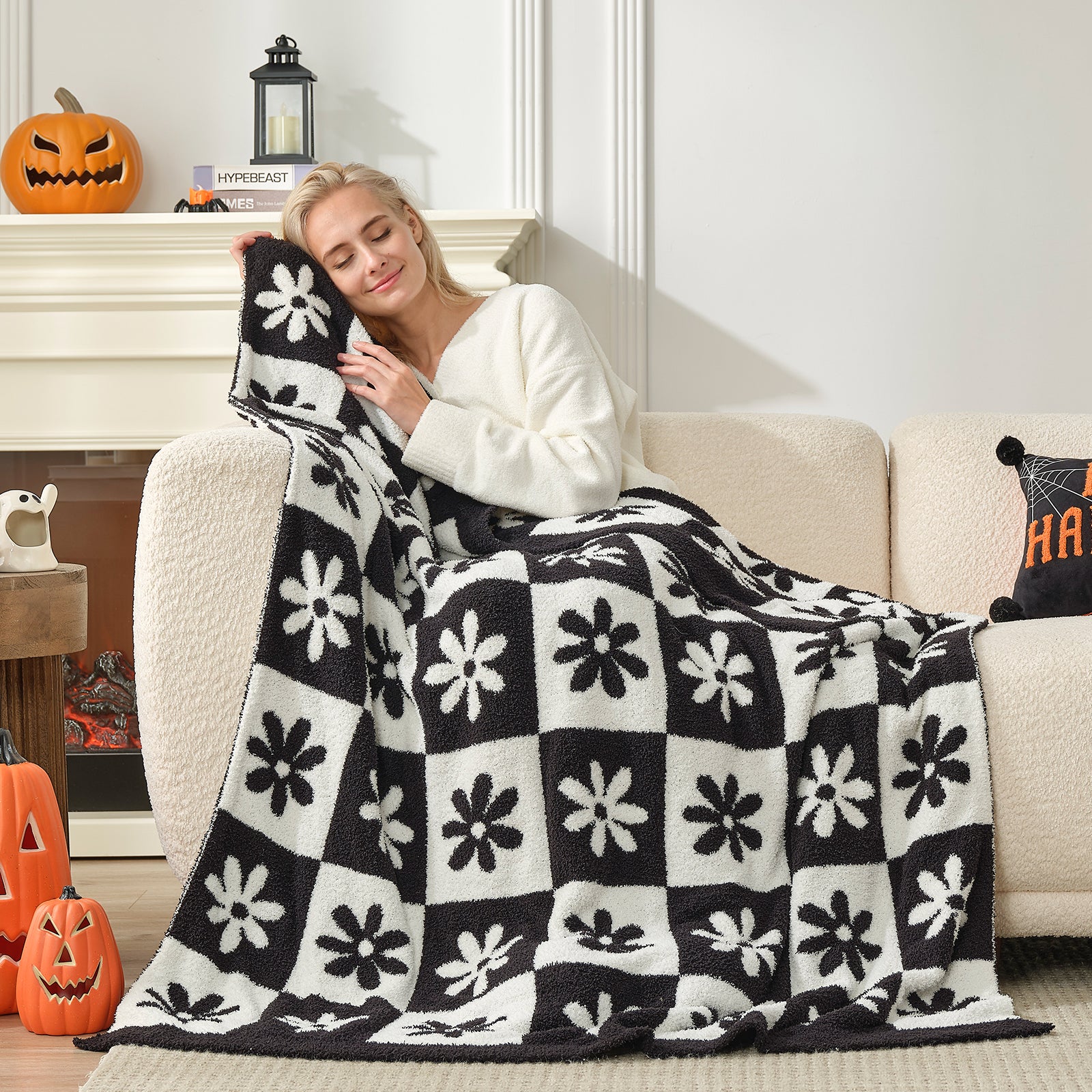 Woman sitting on a couch with a black and white patterned blanket, surrounded by Halloween decorations. #color_Black