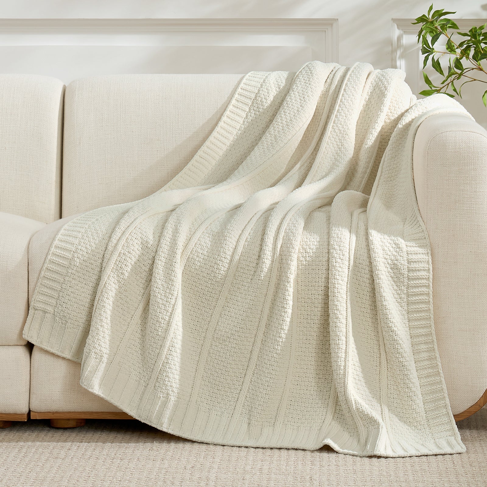 Snuggle Sac ivory textured blanket draped over a beige sofa in a bright room. #color_Ivory