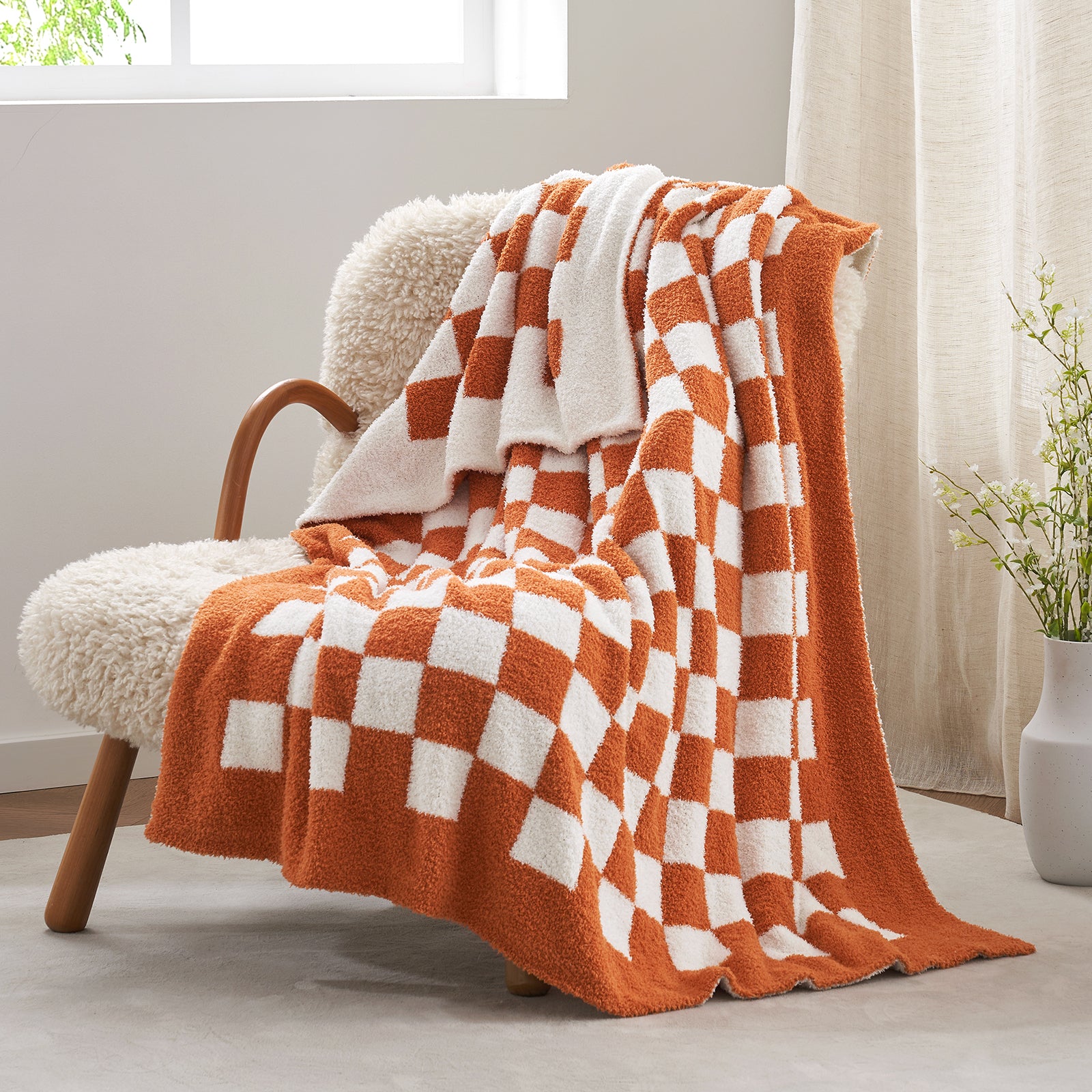 Orange and white checkered blanket draped over a chair in a bright room with curtains. #color_Checkered Burnt Orange