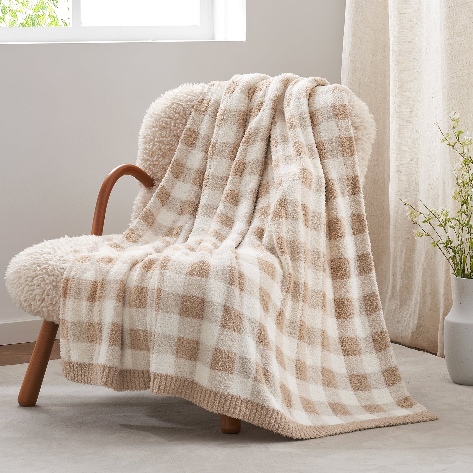 Plaid blanket draped over a chair in a cozy room with a plant and window in the background. #color_Plaid Beige
