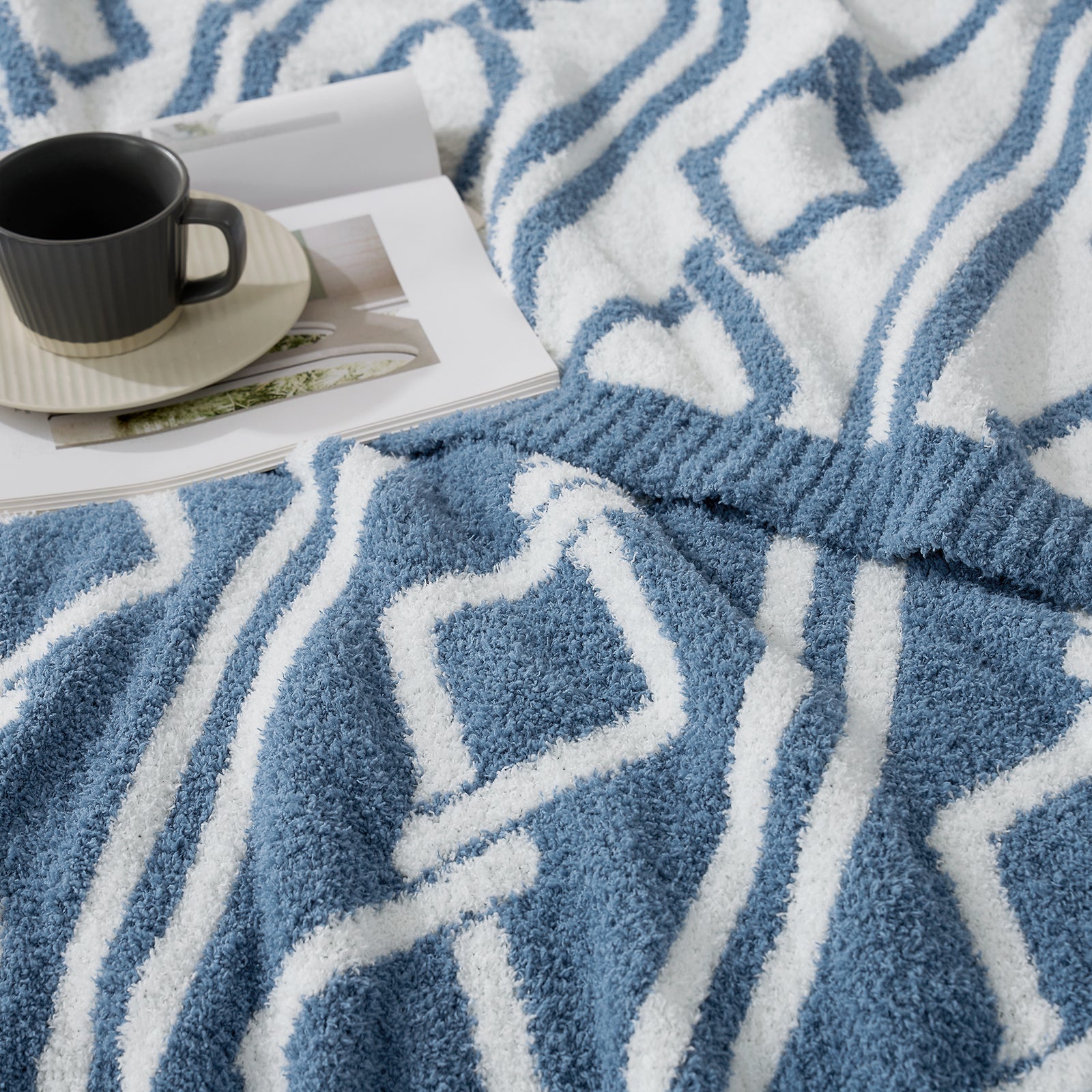Close up of Snuggle Sacs Aesthetic Boho Feather Yarn Knit Throw Blanket with a mug and book on the bed#color_Blue