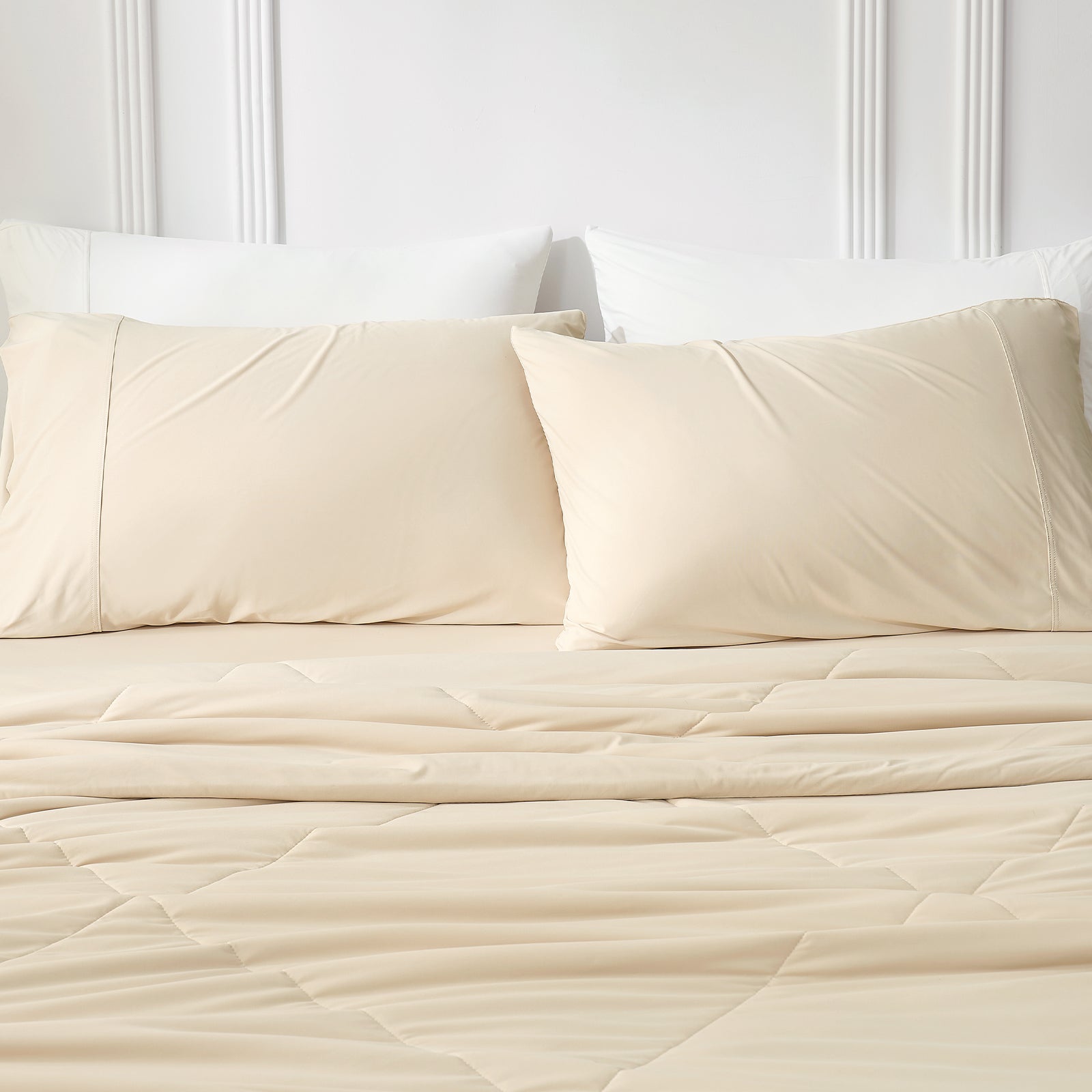Snuggle Sac Khaki quilted bedspread and pillows on a bed with a white headboard.#color_Khaki