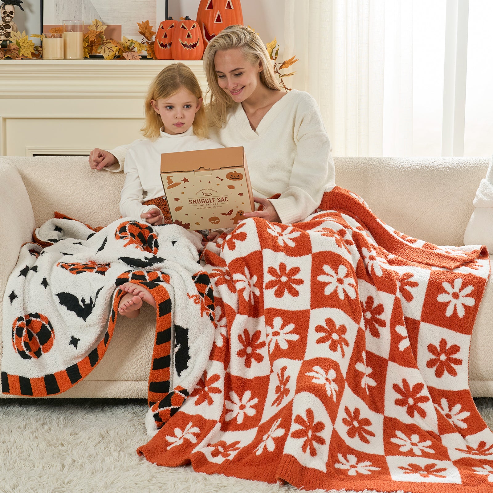 Woman and child sitting on a couch with Halloween-themed blankets and decorations. #color_Orange