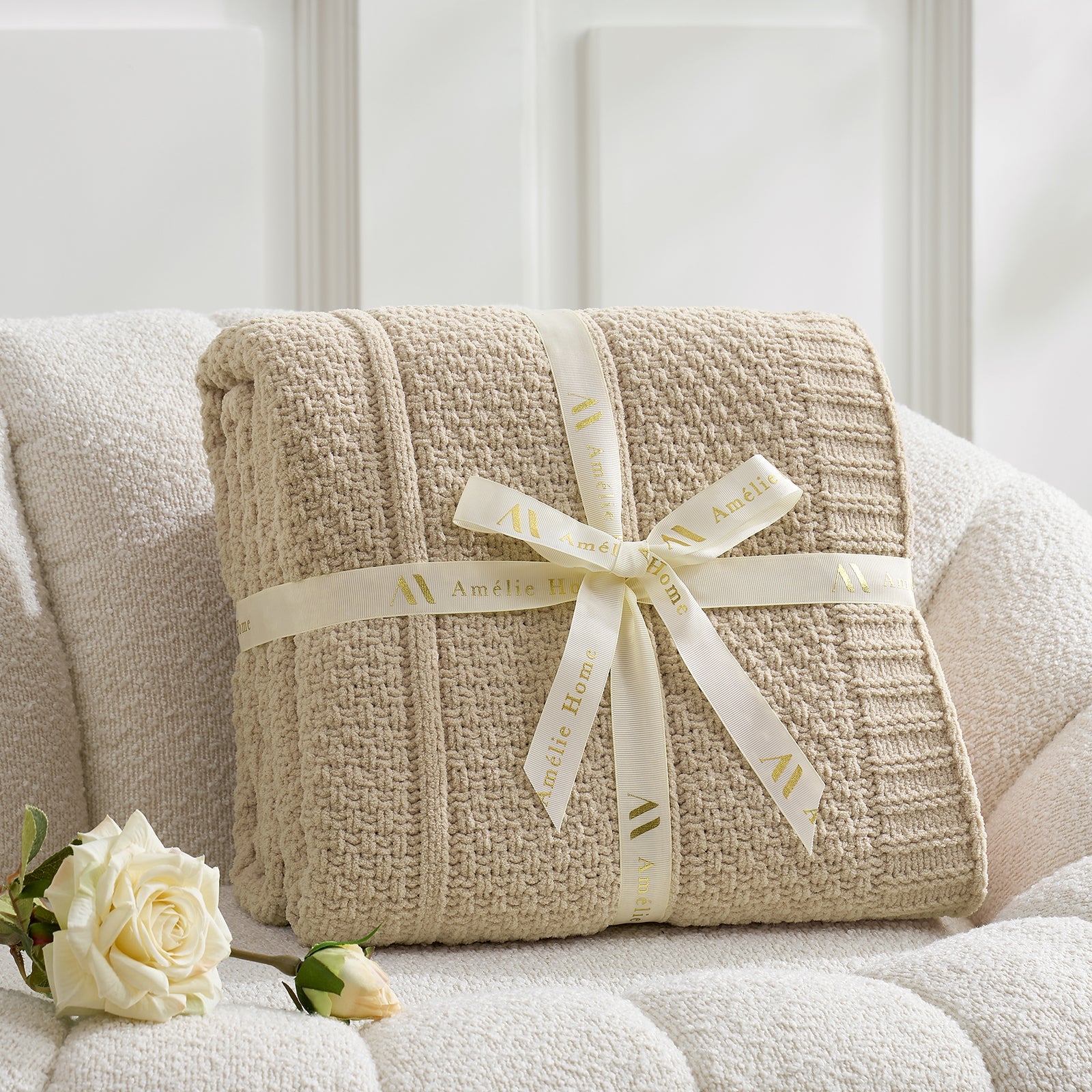 Beige textured blanket with a ribbon on a white couch, accompanied by white roses. #color_Beige