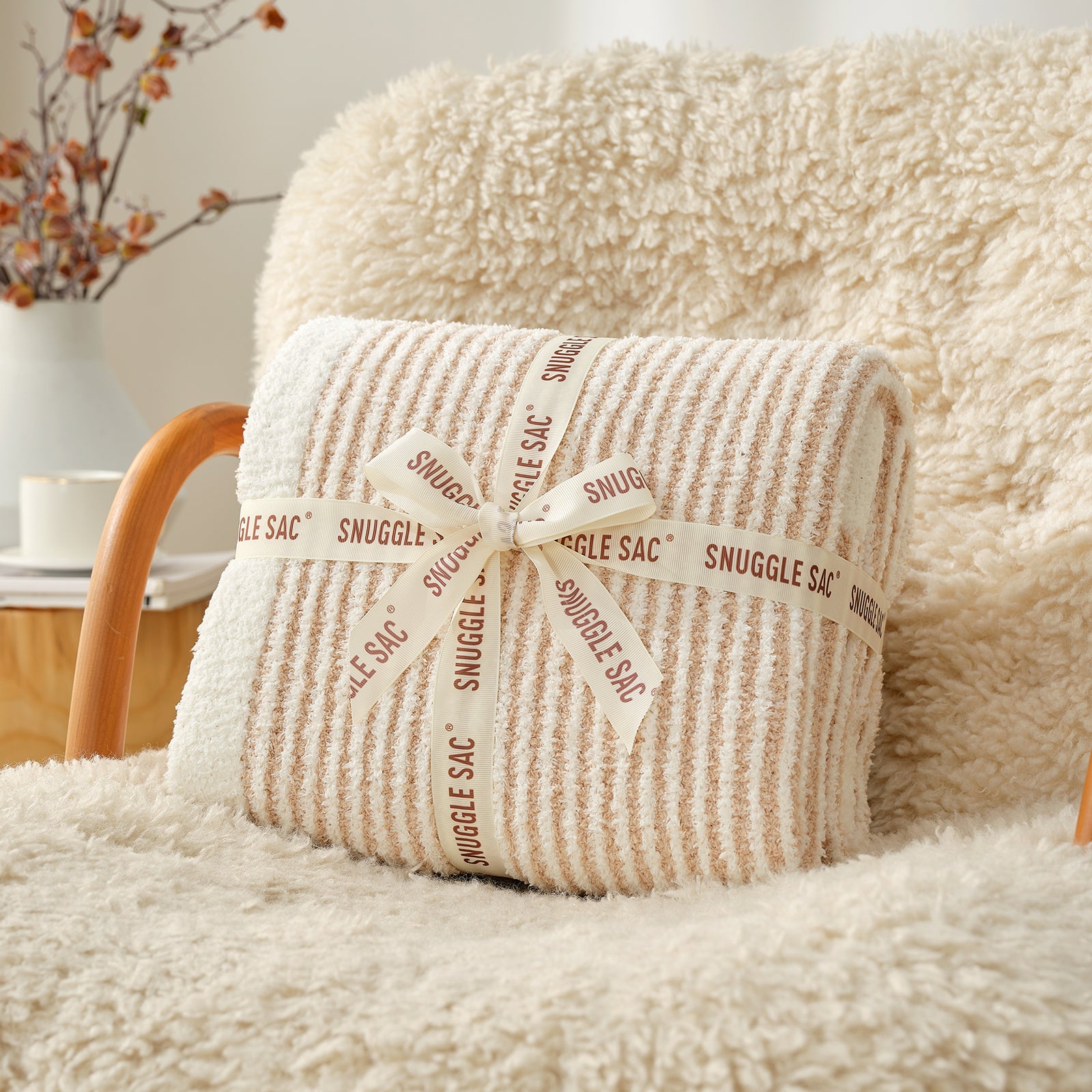 Folded beige blanket with 'Snuggle Sac' label on a fluffy chair #color_Cream/Beige