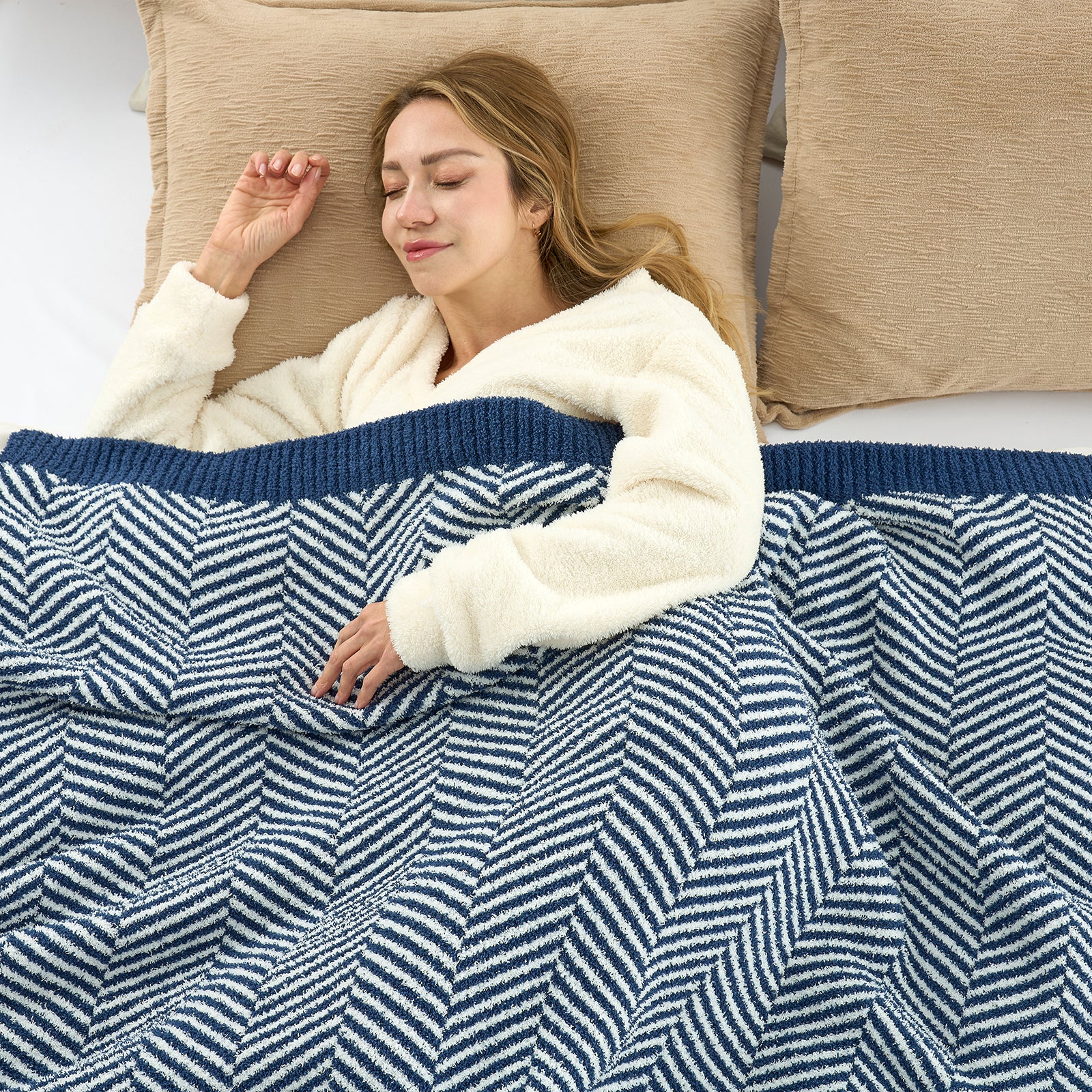 A woman laying down on the bed with Snuggle Sacs Herringbone Feather Yarn Knit Throw Blanket#color_Navy