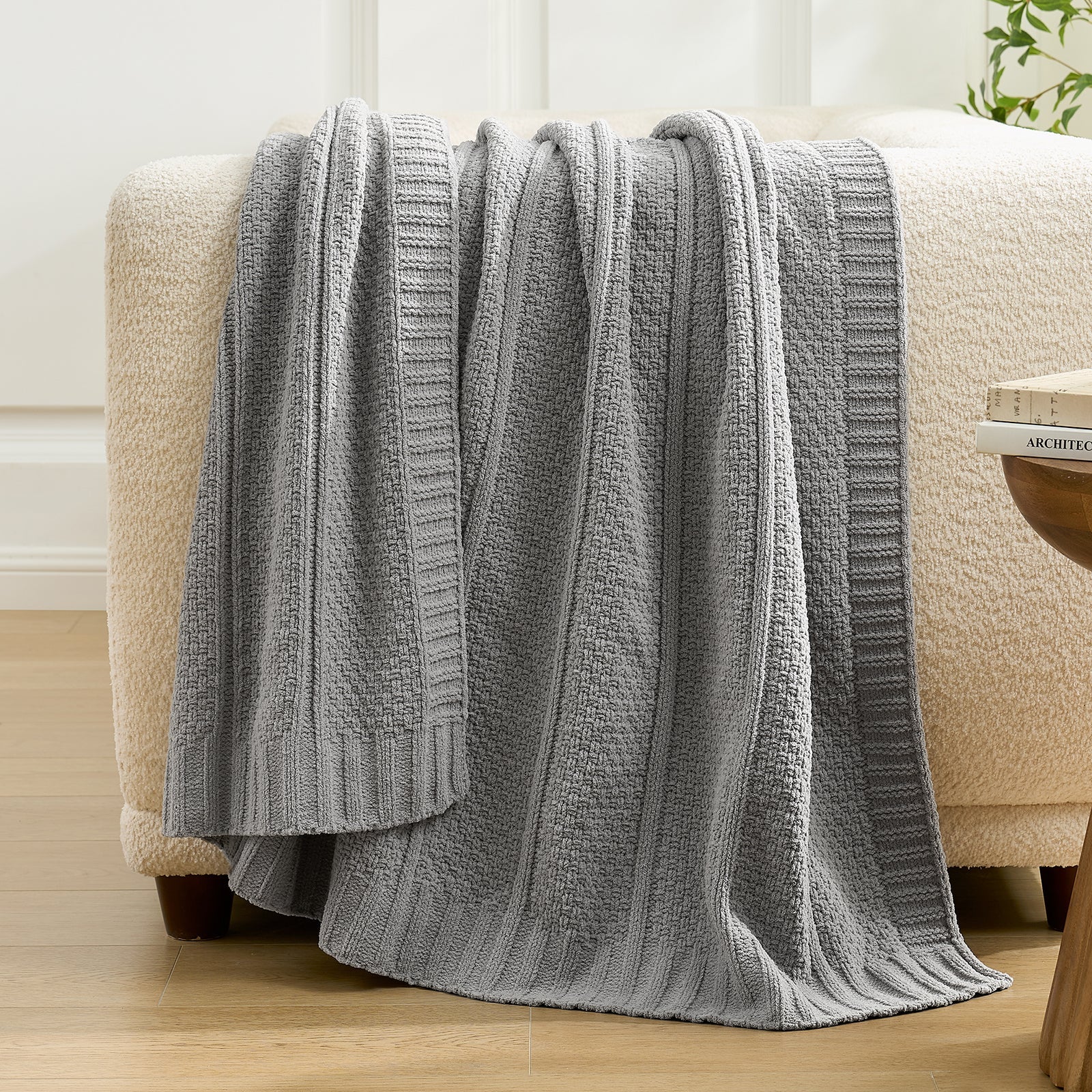 Snuggle Sac gray textured blanket draped over a beige armchair in a room with light-colored walls and a plant. #color_Gray