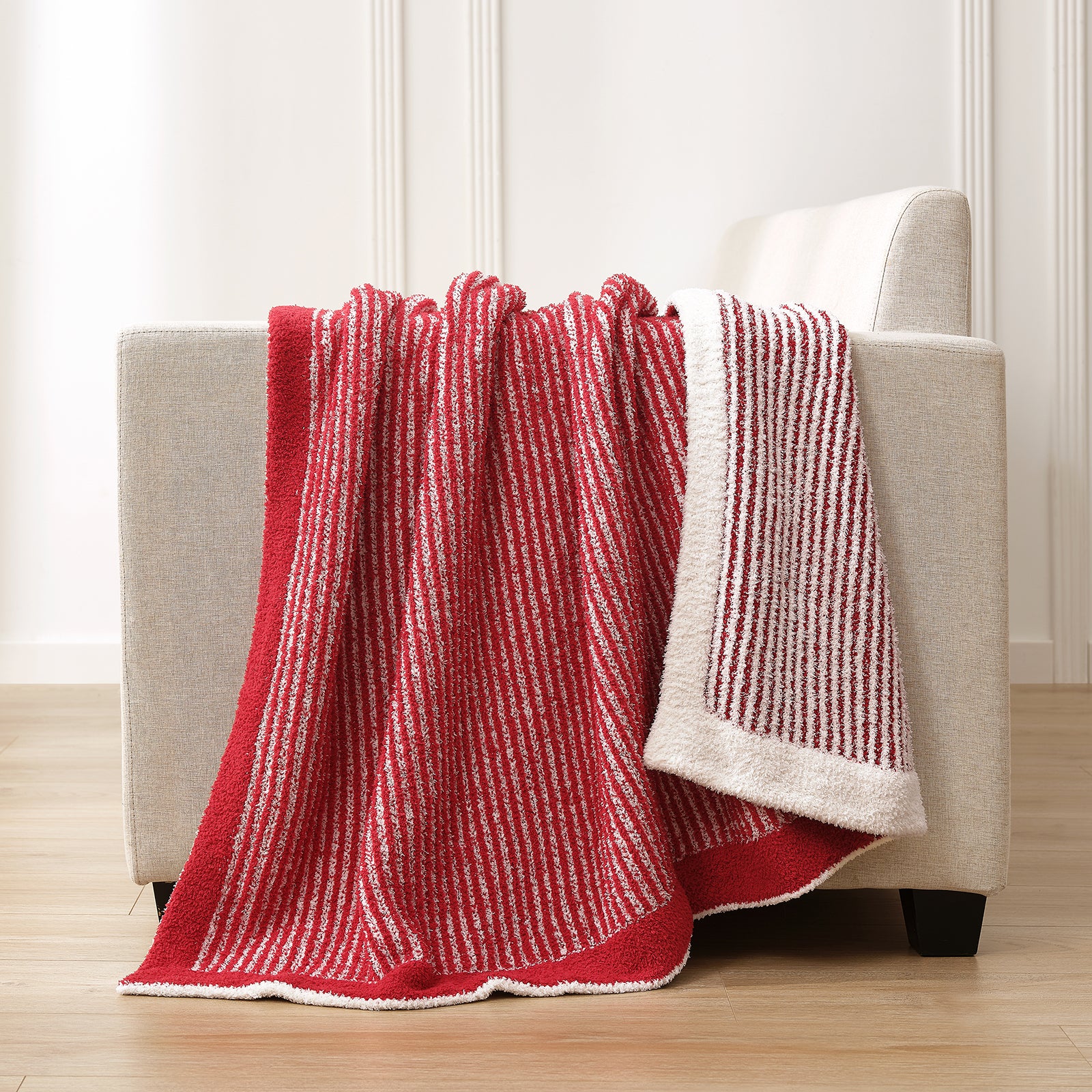 Red and white striped blanket draped over a gray armchair in a room with wooden flooring. #color_Red/Cream