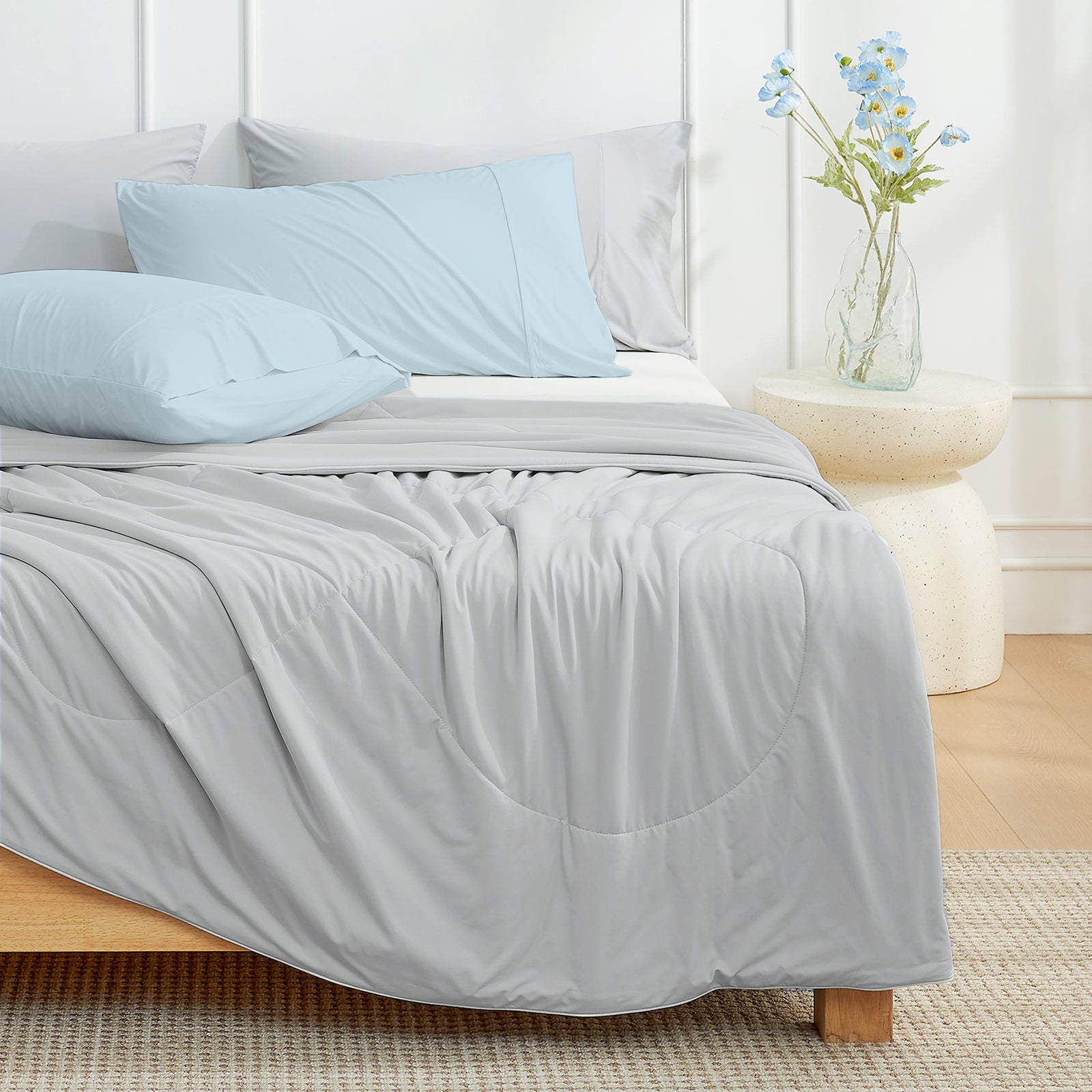 Gray cooling comforter on a bed with blue pillows in a bedroom setting.#color_Grey
