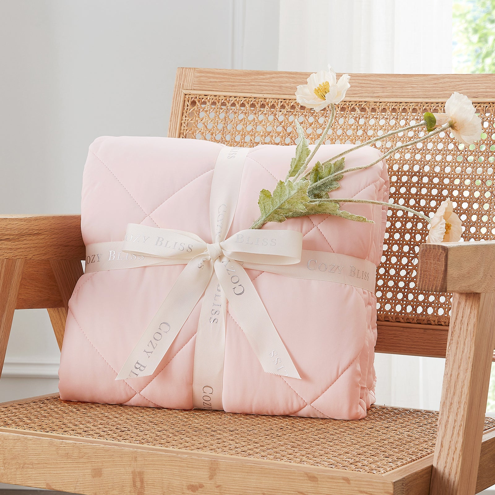 Folded comforter with white ribbon on chair surrounded by plants, presented as a perfect gift#color_Pink