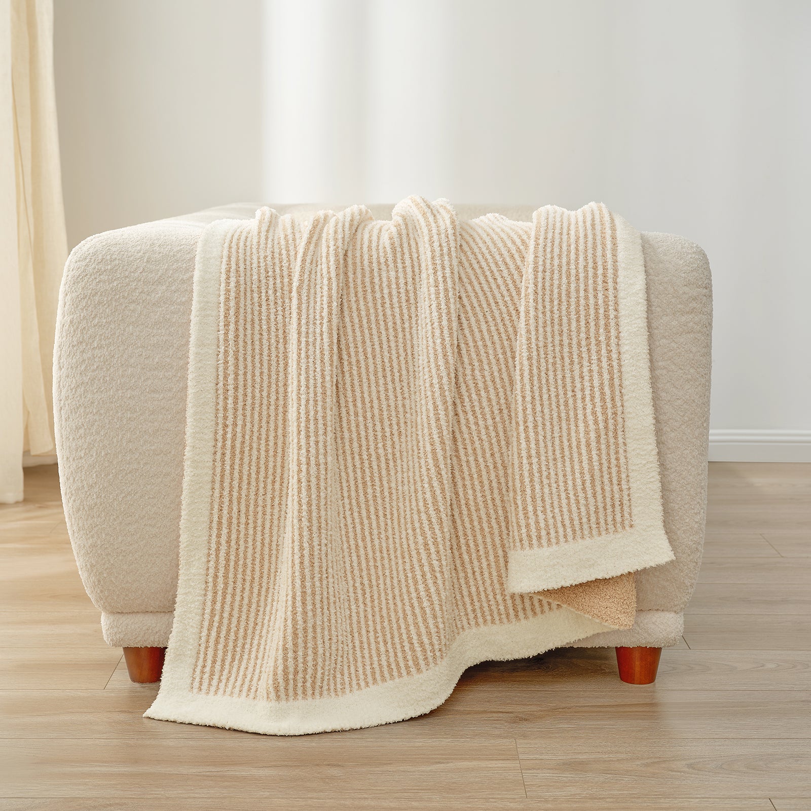 Beige textured blanket draped over a small ottoman on a wooden floor. #color_Cream/Beige