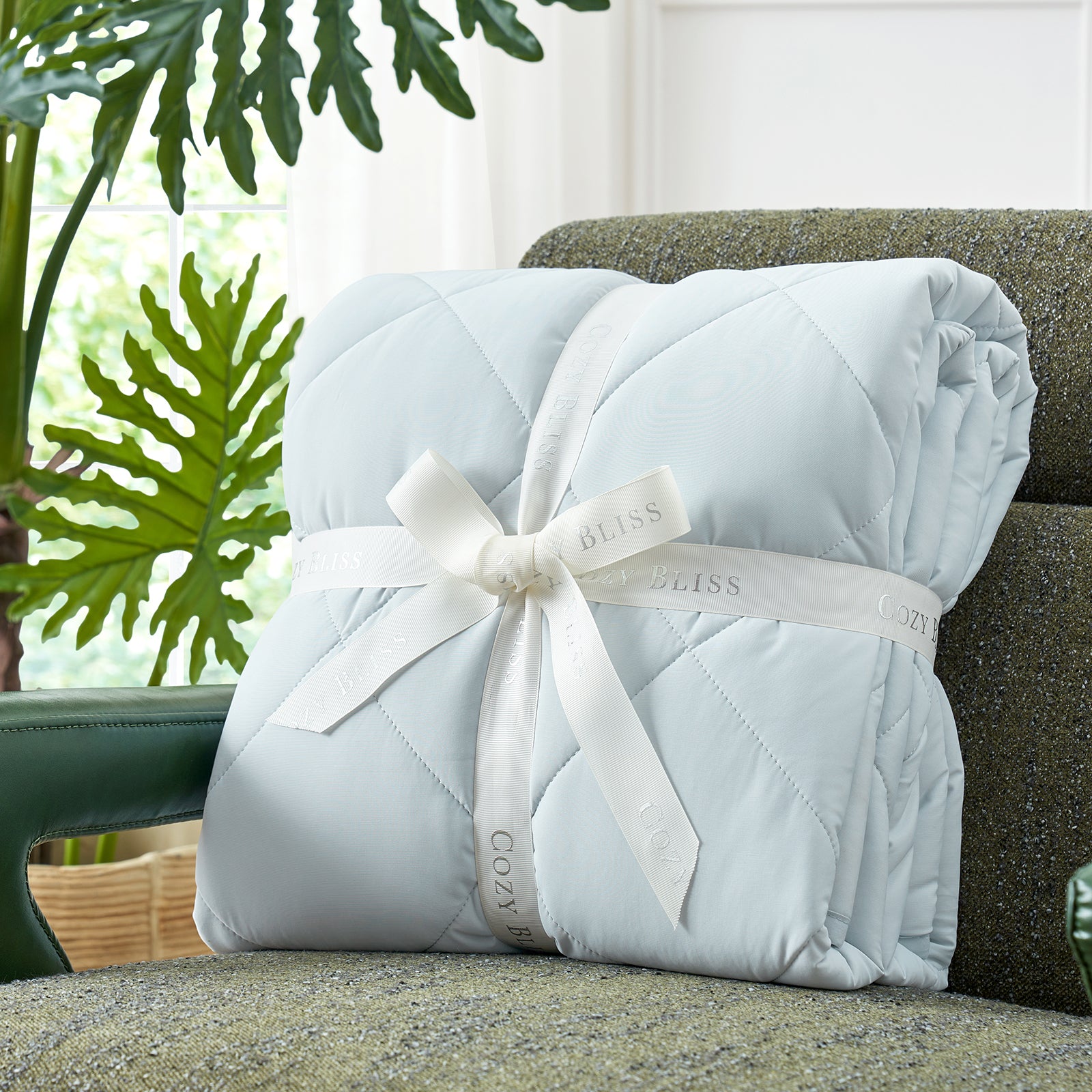 Folded comforter with white ribbon on green couch surrounded by plants, presented as a perfect gift#color_Blue