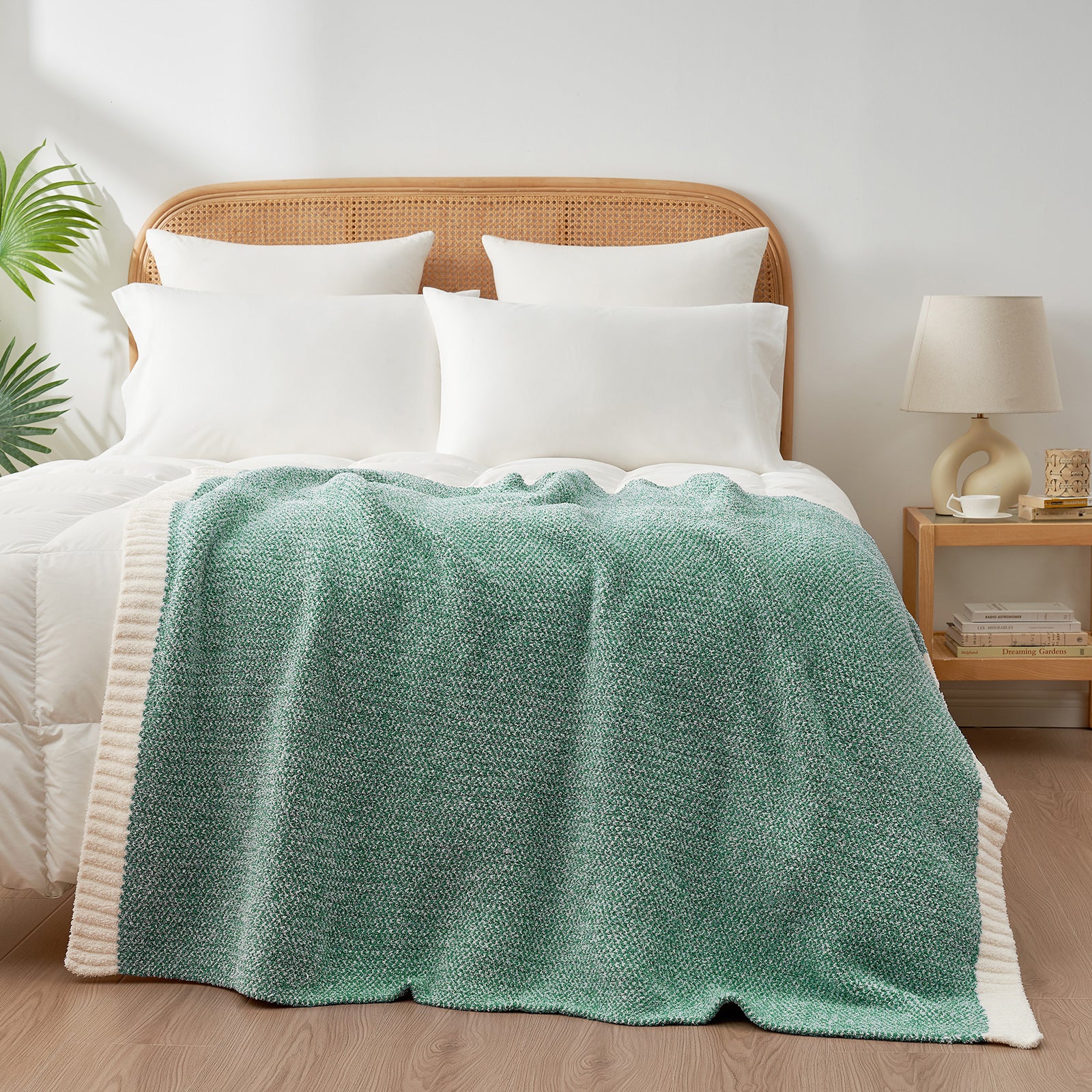 Bed with white bedding and a green blanket, wooden headboard, and side table with lamp. #Color_Heather Green