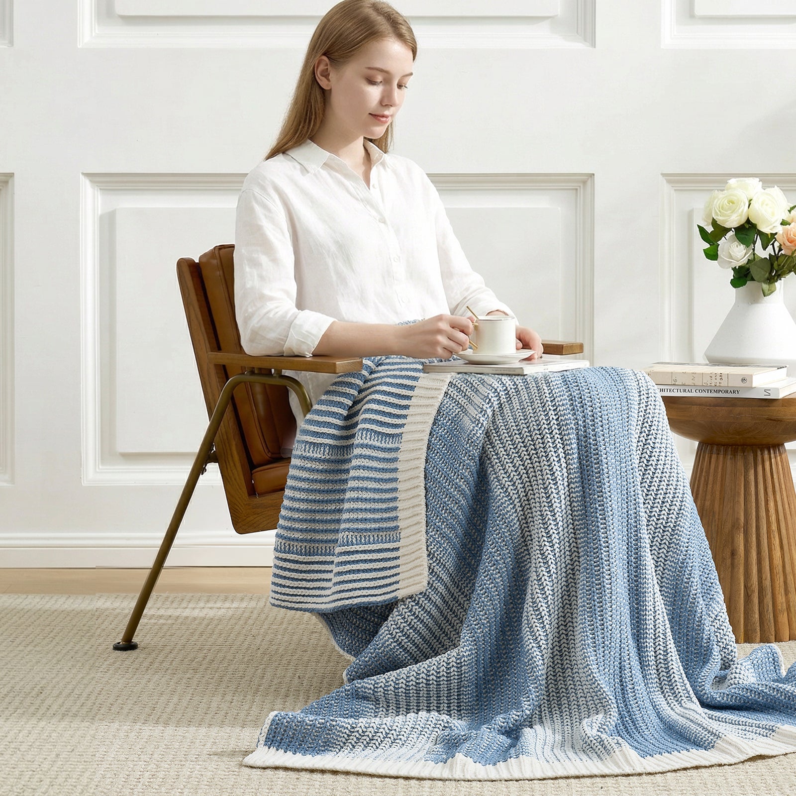Woman sitting on a chair with a blue and white striped blanket draped over her lap in a room with wooden flooring and white walls. #color_Two-tone Blue