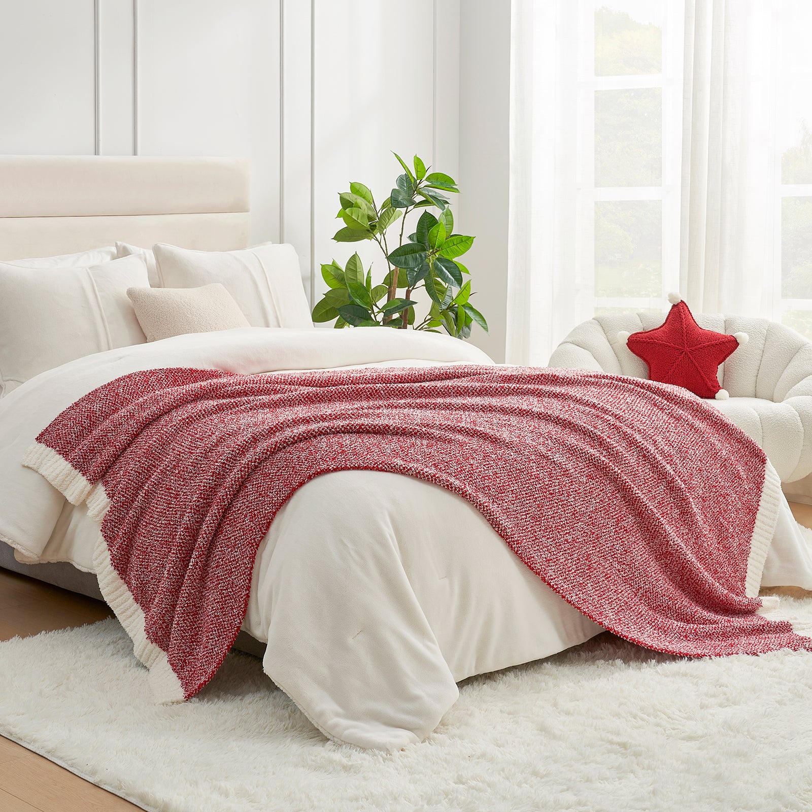 Red blanket draped over a bed in a bright bedroom with white walls and a plant.  #color_Heather Red