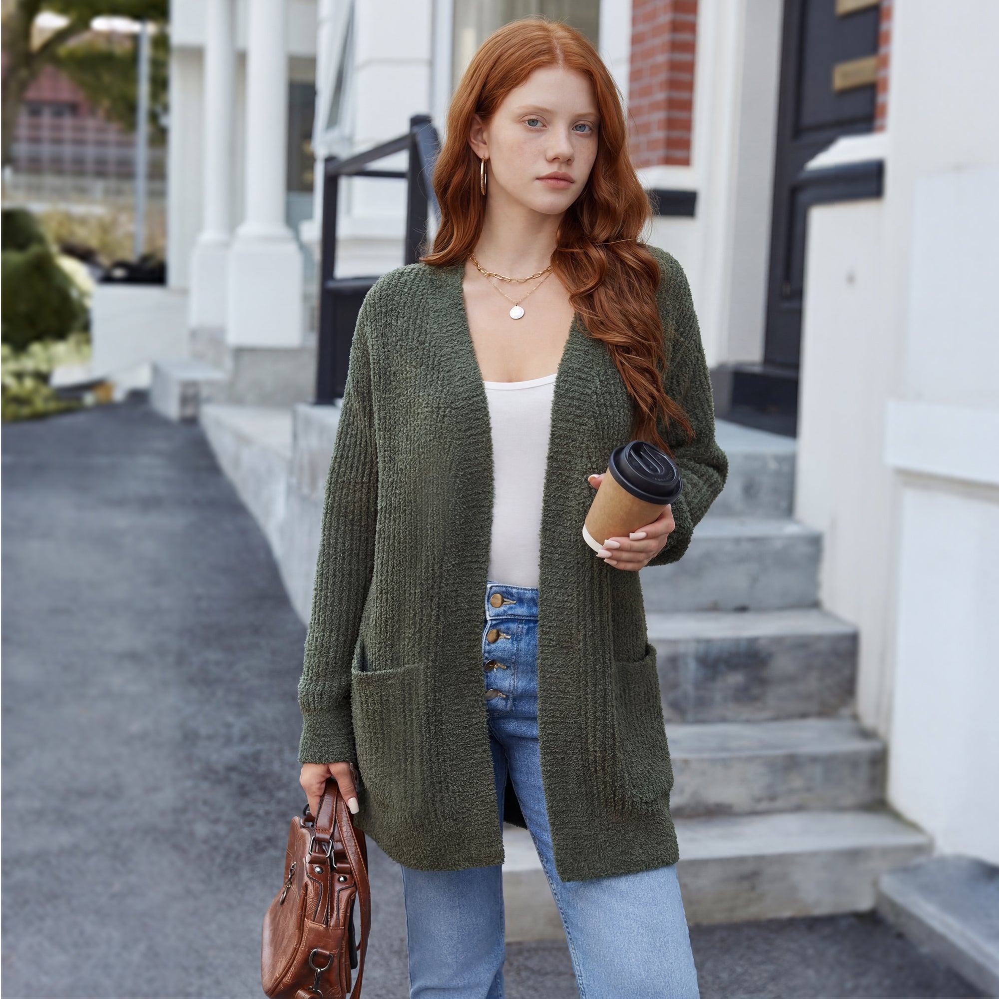 Woman wearing a green cardigan, white top, and blue jeans, holding a coffee cup and a handbag, standing on steps.#color_Army Green