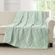 Snuggle Sac Green cooling blanket draped over a beige sofa in a room with large windows.#color_Mint Green