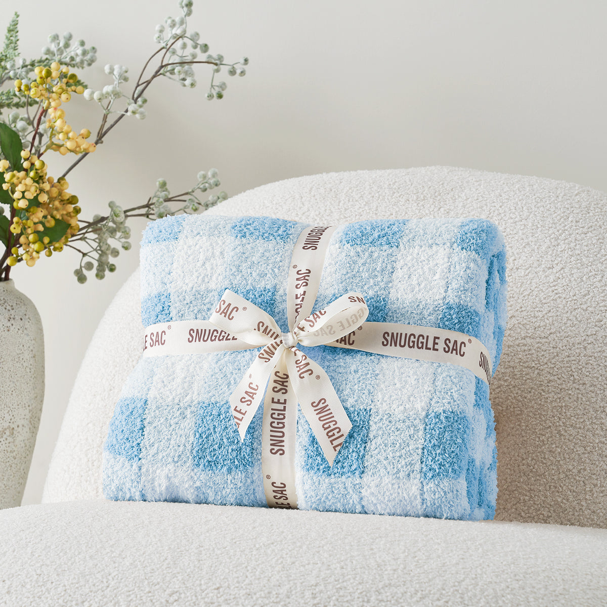 Plaid-patterned Snuggle Sac wrapped with a ribbon on a gray chair. #color_Ice Blue