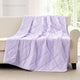 Snuggle Sac Purple cooling blanket draped over a beige sofa in a room with large windows.#color_Purple