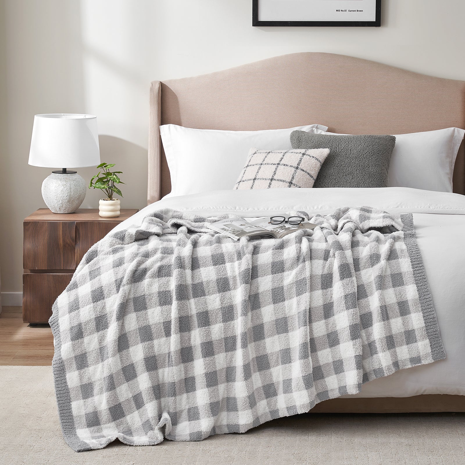 Bedroom with a bed featuring a gray and white checkered blanket, pillows, and a wooden nightstand with a lamp. #color_Plaid Grey