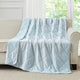 Snuggle Sac Blue cooling blanket draped over a beige sofa in a room with large windows.#color_Blue