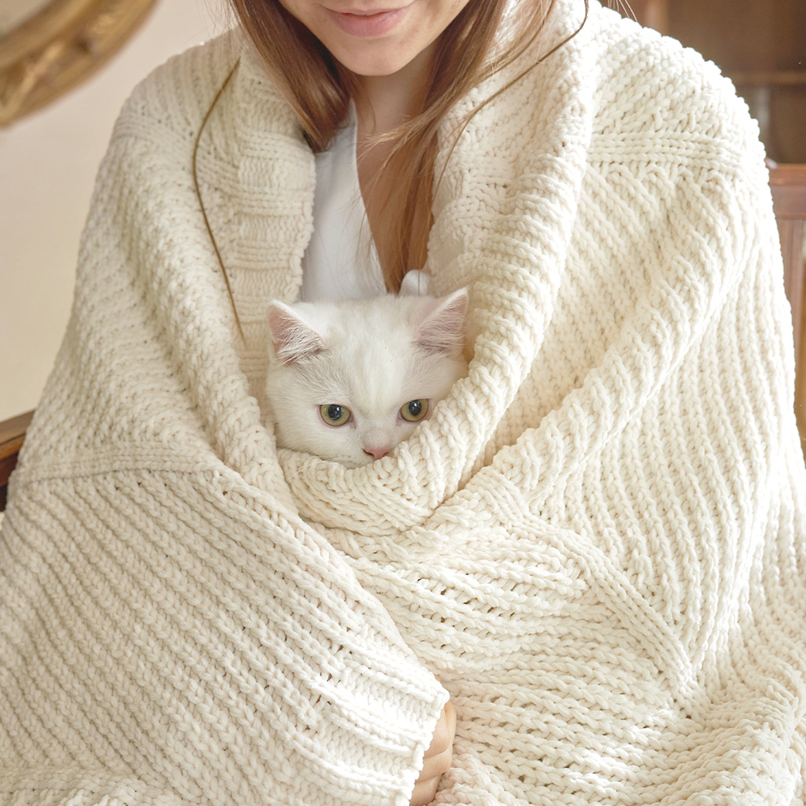 Woman wrapped in a chevron chenille knit throw blanket in Ivory holding a cat for warmth #color_Ivory