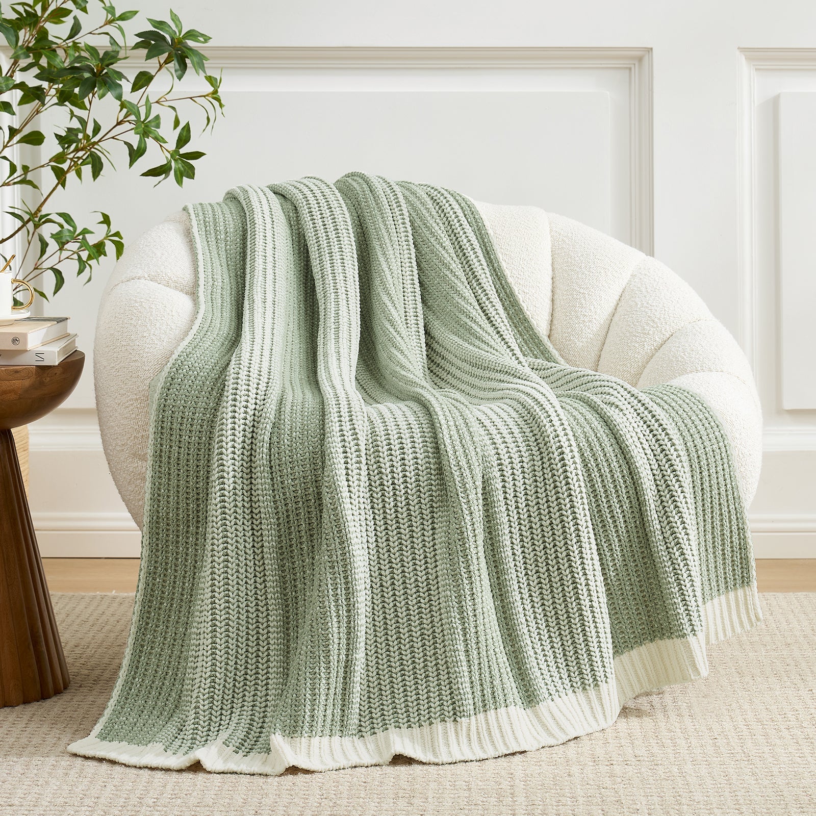 Green knitted blanket draped over a white armchair in a room with a plant and side table. #color_Two-tone Green