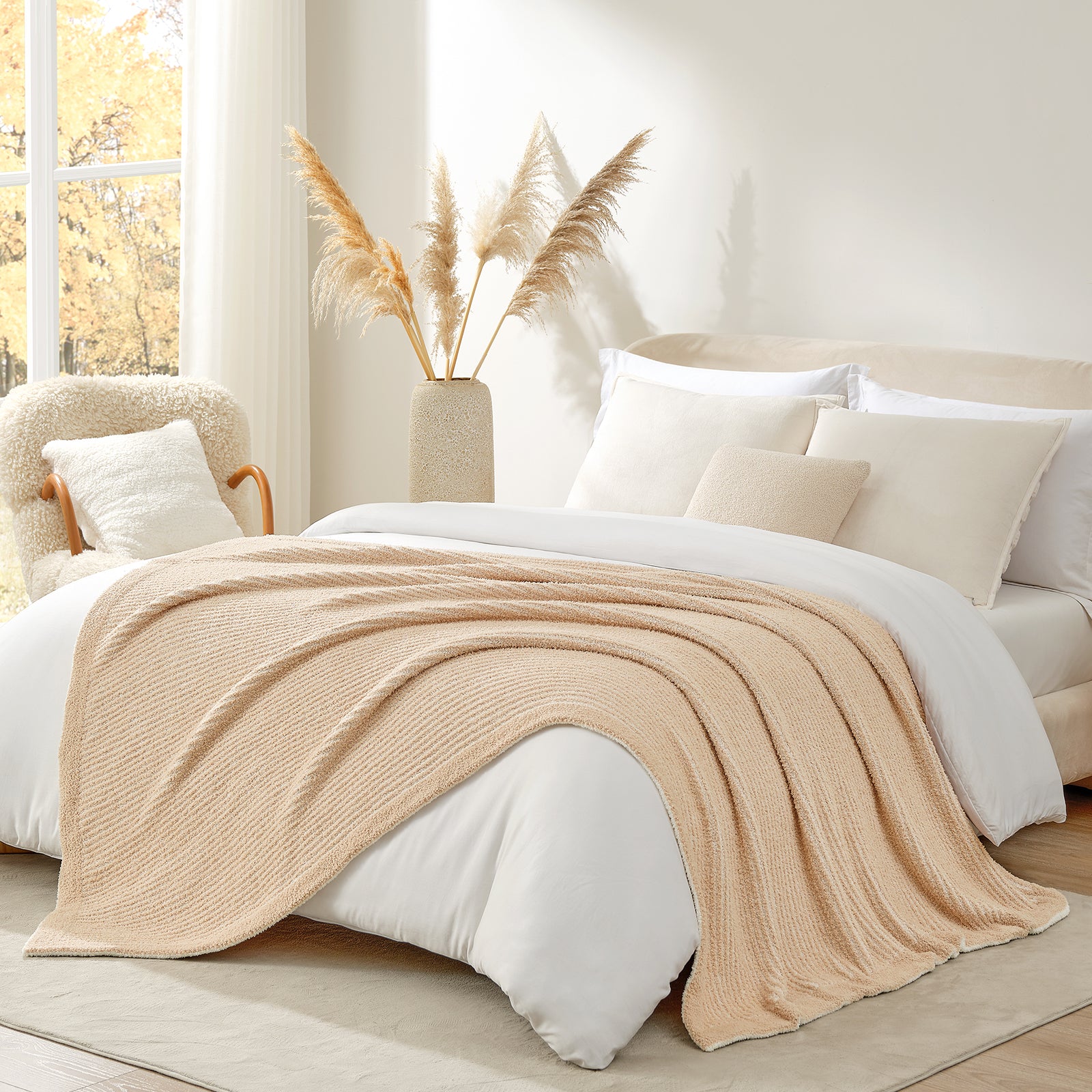 Beige blanket draped over a bed in a cozy bedroom with a vase of pampas grass.#color_Cream/Beige
