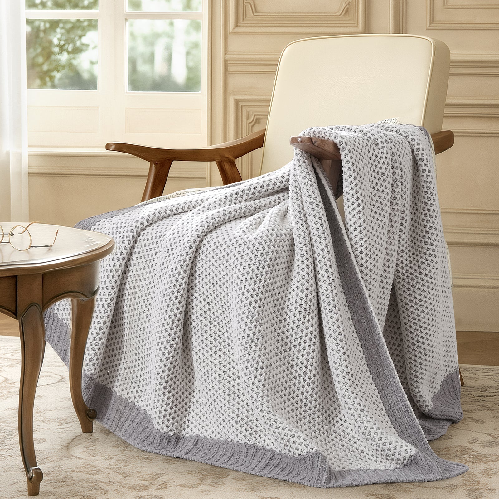 Gray patterned throw blanket draped over a wooden armchair in a room with a window and table. #color_Gray&White
